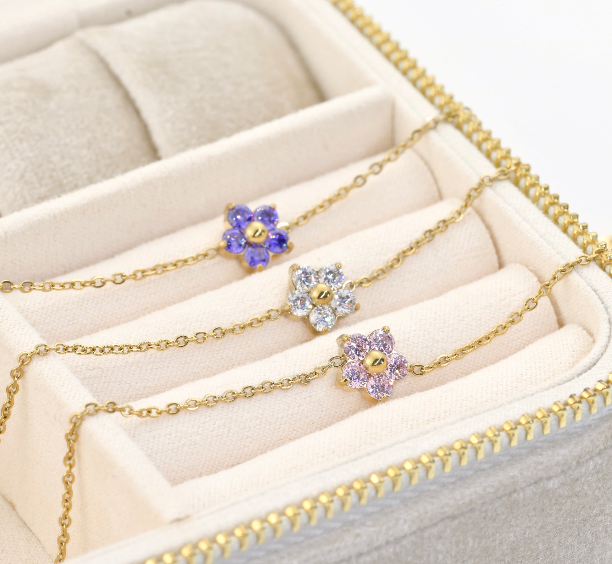 Gold bracelets with floral charms  featuring different colored stones on a beige jewelry box