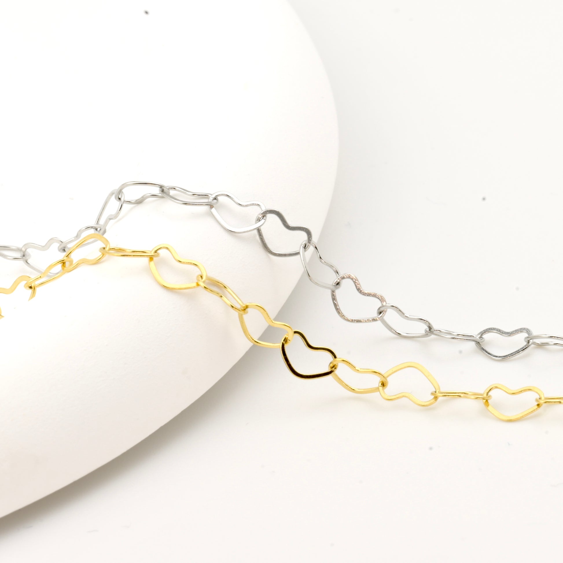 Two heart-shaped chain bracelets, one gold and one silver, on a white surface.