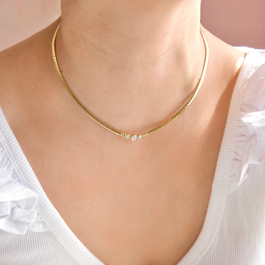 A close-up of a model wearing a delicate gold chain necklace with three small clear rhinestones at the center, styled with a white ruffled top.