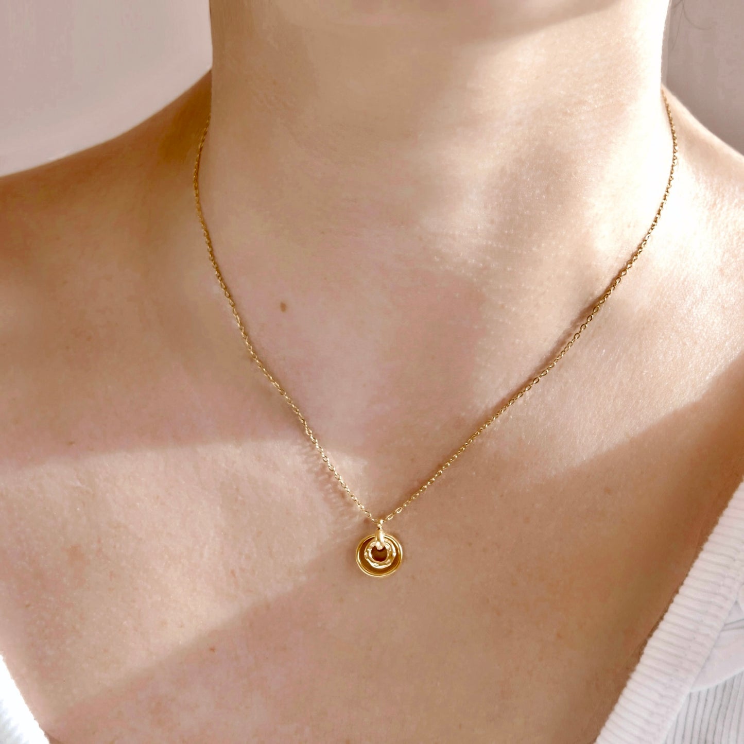 A close-up of a person's neck and upper chest wearing a delicate gold chain necklace with a small circular pendant.