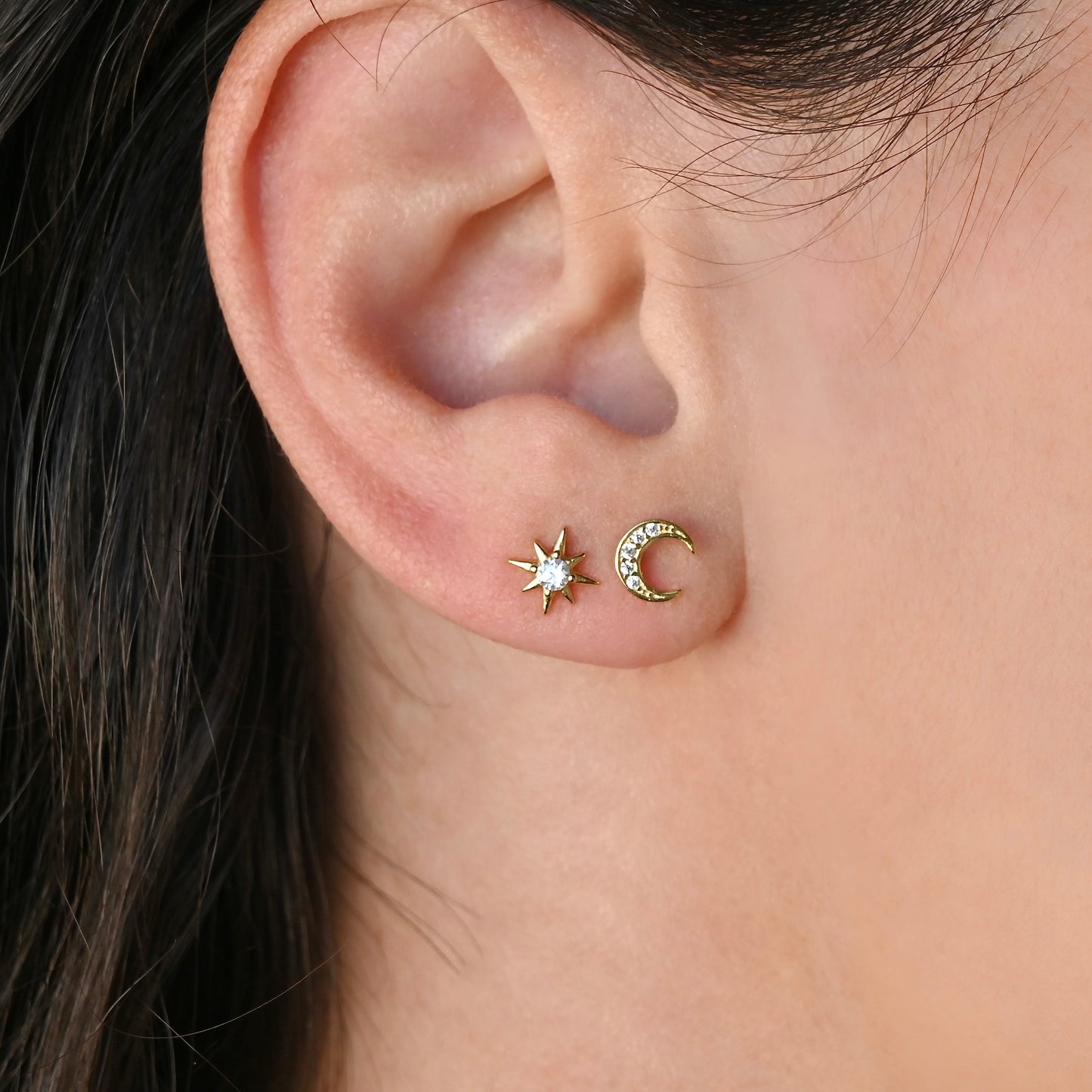 Close-up of an ear wearing small gold star and moon earrings.