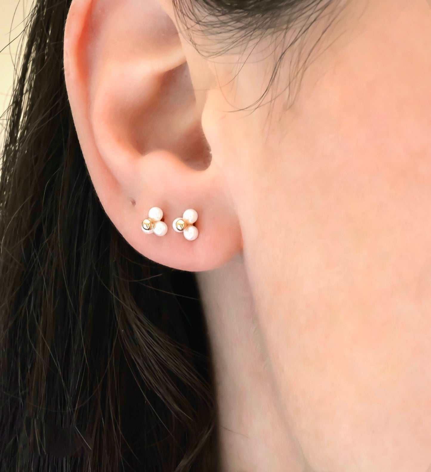Close-up of an ear wearing two triplepearl cluster earrings with rose gold posts.