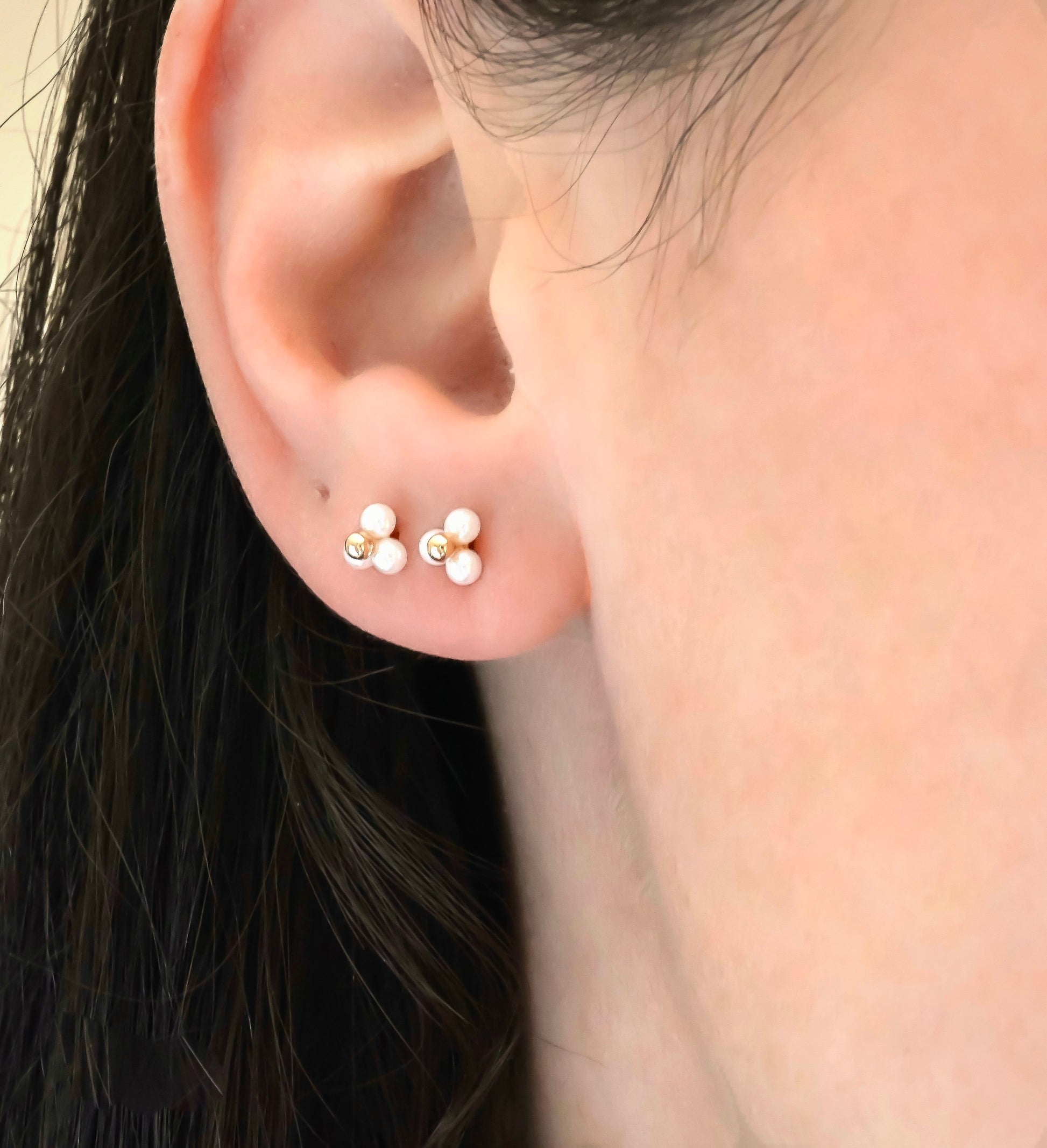 Close-up of an ear wearing two triplepearl cluster earrings with rose gold posts.