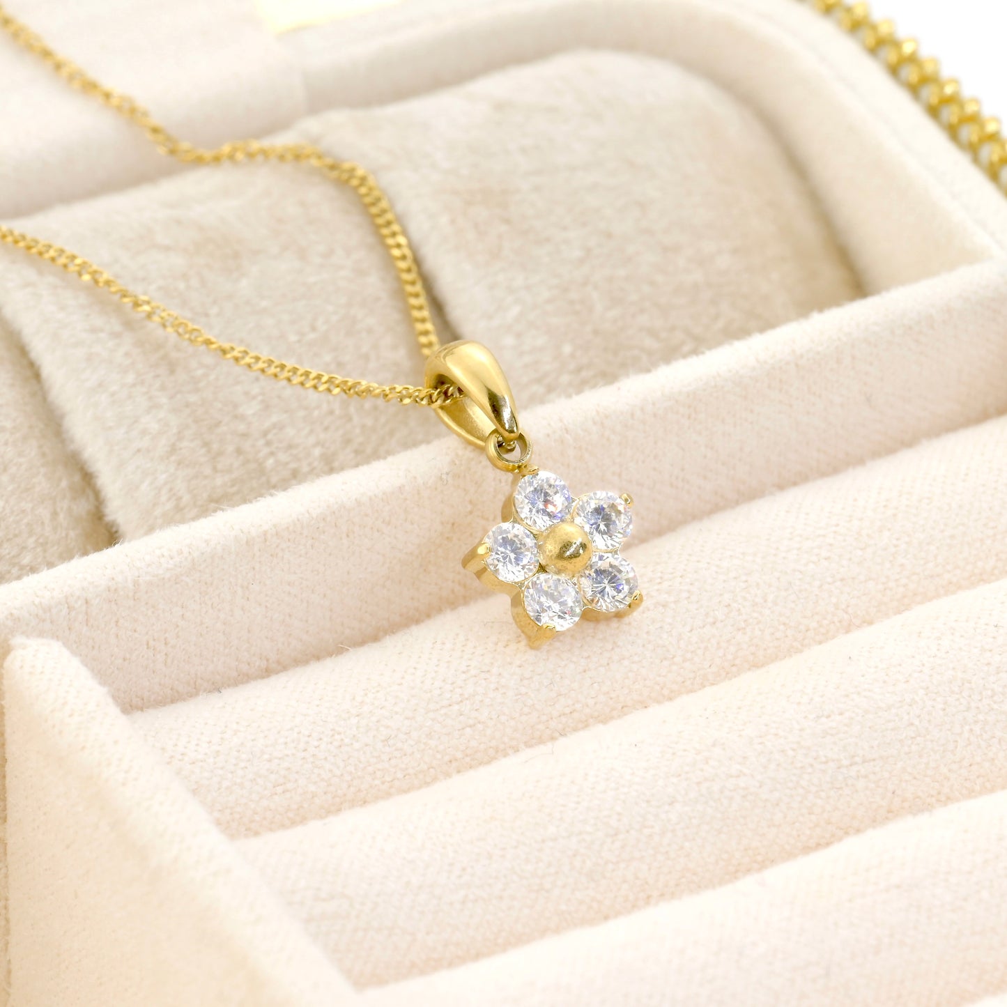 Gold necklace with a diamond flower pendant on a beige velvet surface
