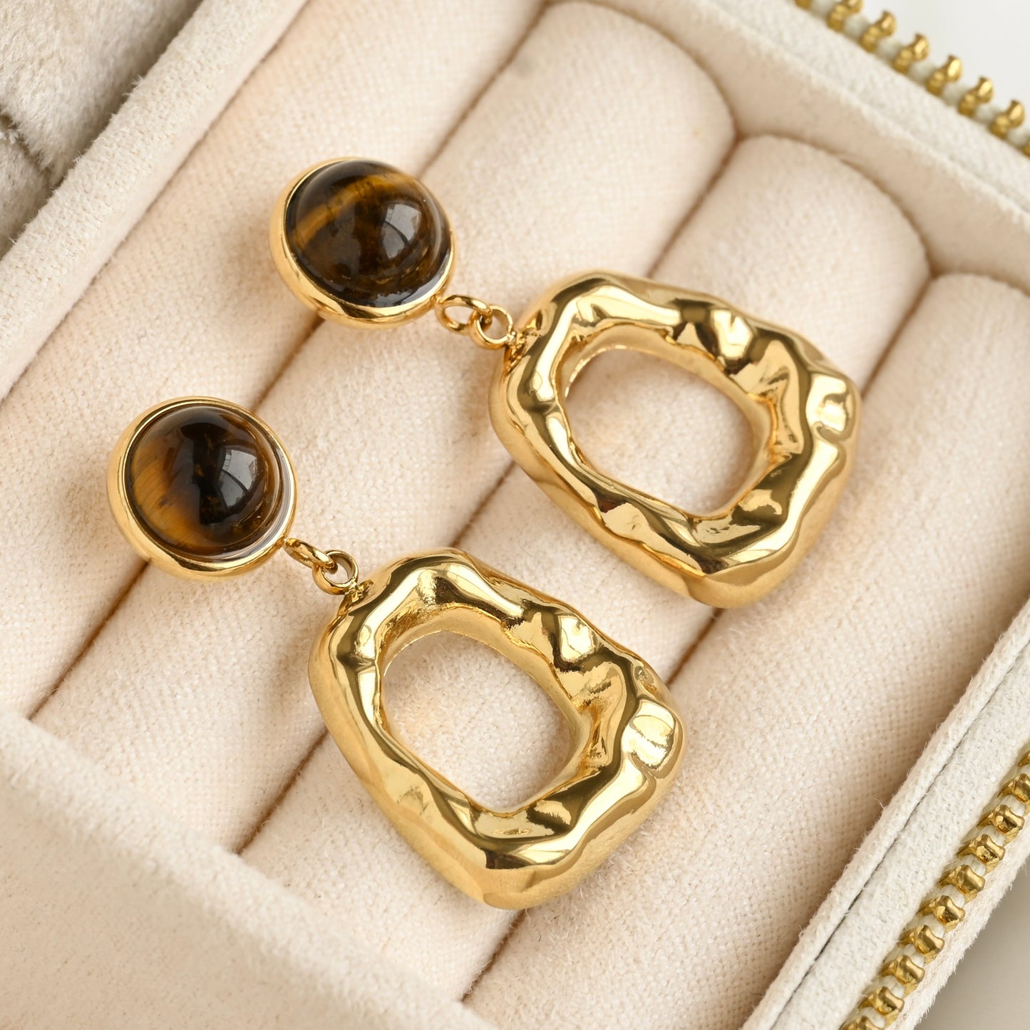Organic gold dangle earrings with brown gemstones on a beige jewelry box