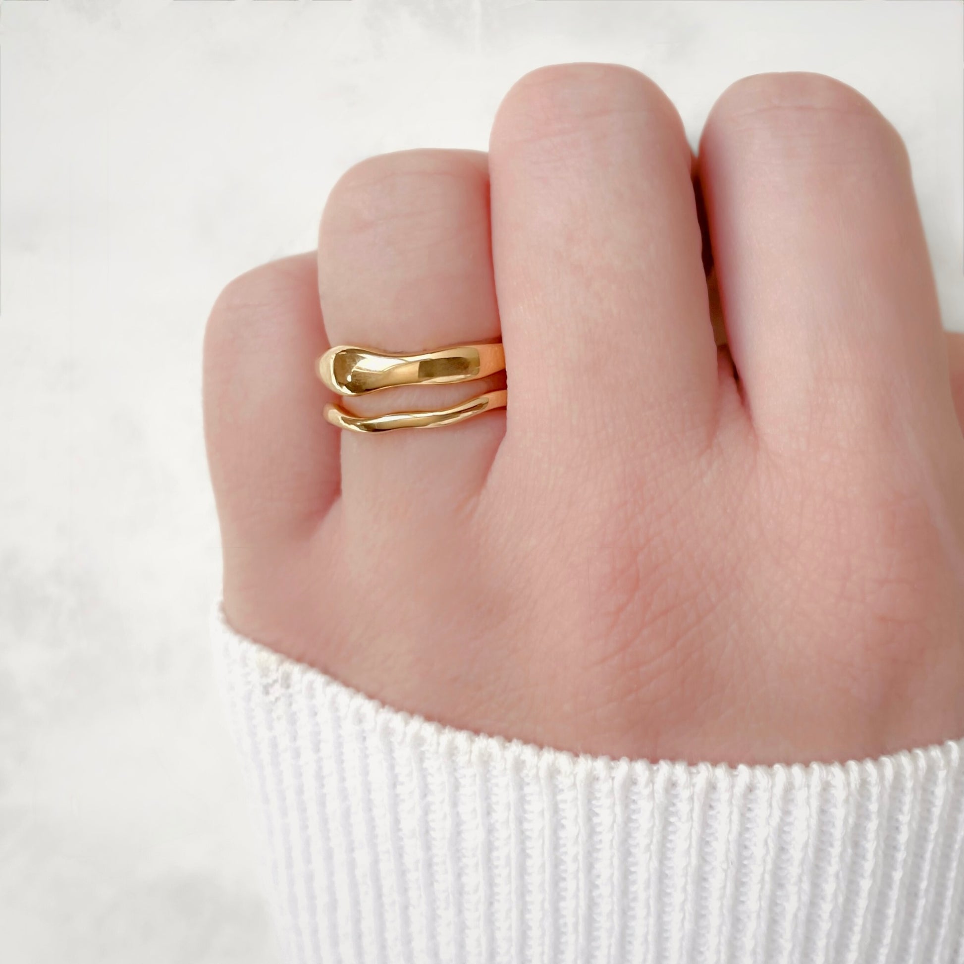 Gold ring set on the same finger, a thin wavy band and a thicker one stacked on top against a white background