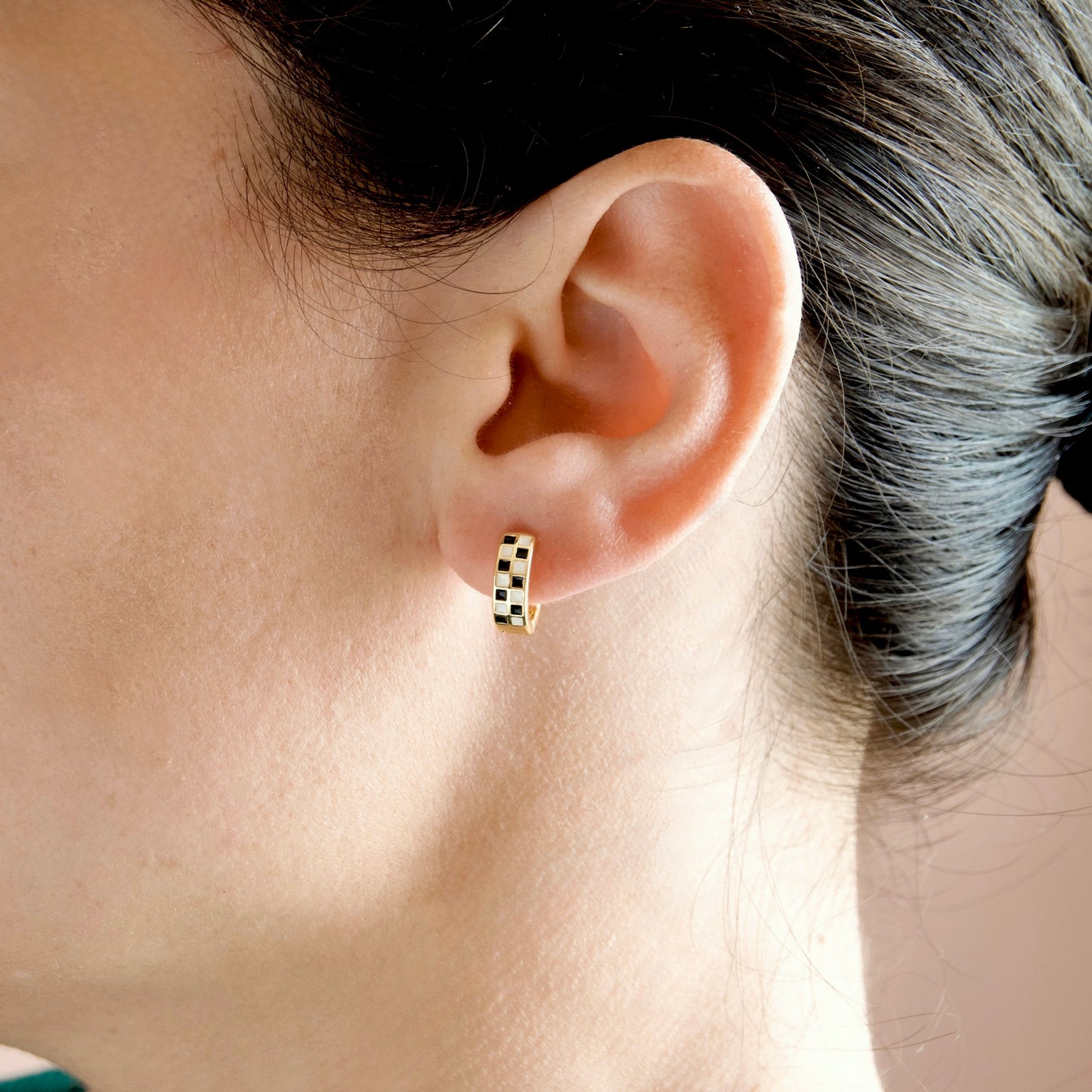 A close-up of a person's ear wearing a small gold hoop earring with a black and white checkered pattern.