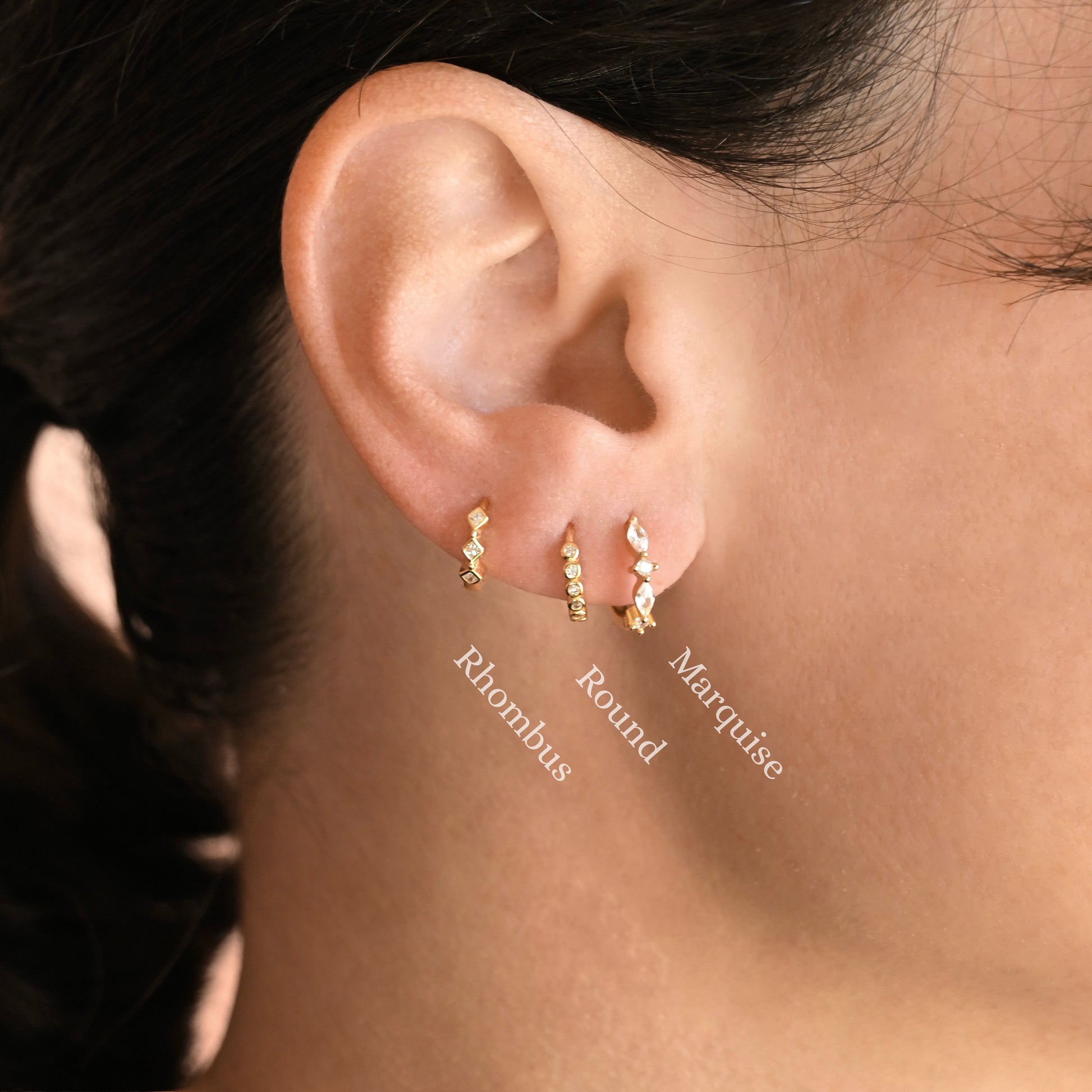Close-up of a person's ear wearing three small gold ear cuffs labeled Rhombus, Round, and Marquise, with the names overlaid on the photo.