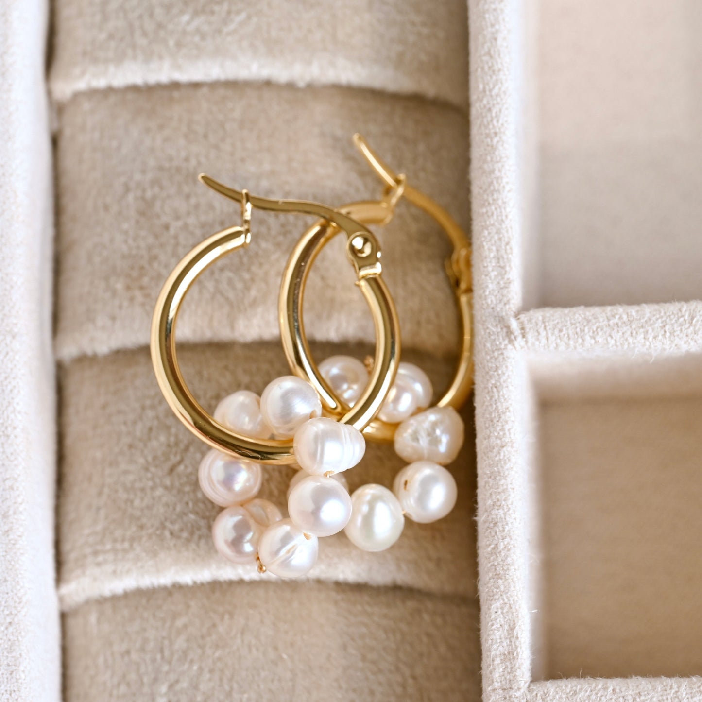 Gold hoop earrings with pearls on a textured beige surface