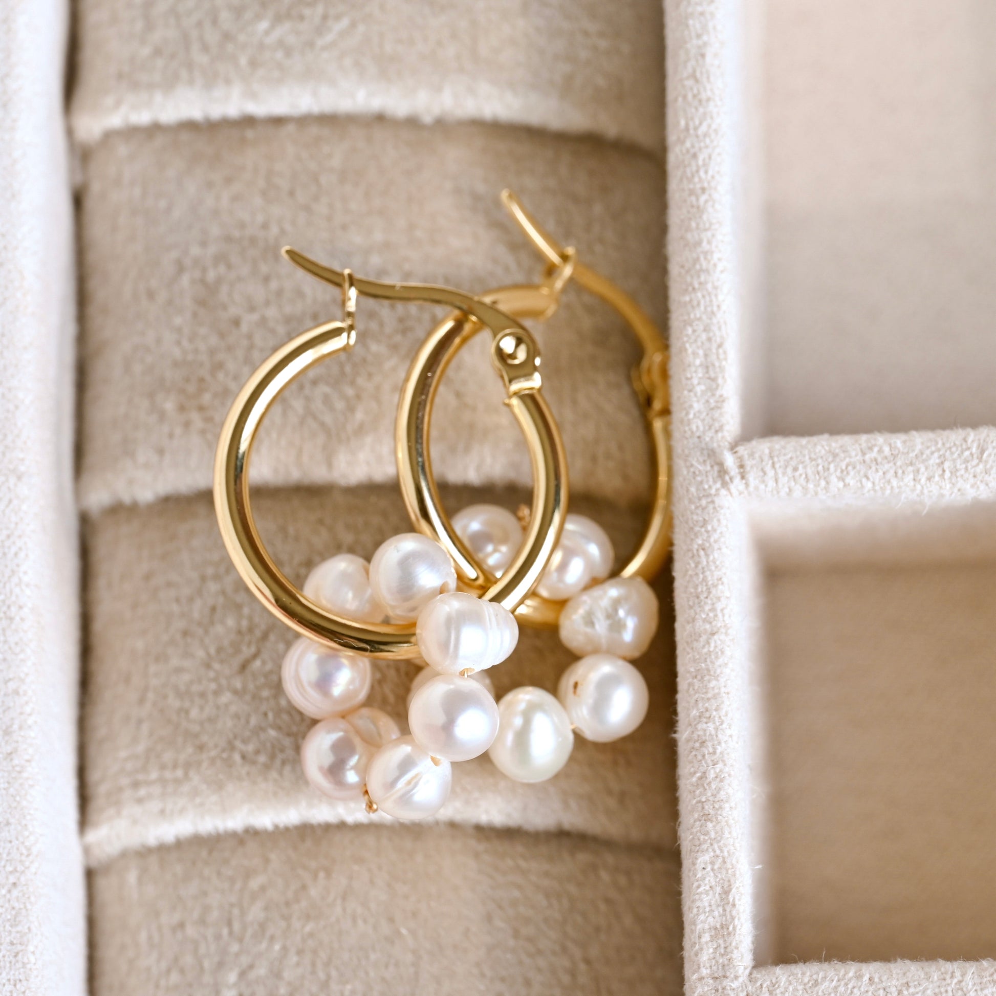 Gold hoop earrings with pearls on a textured beige surface