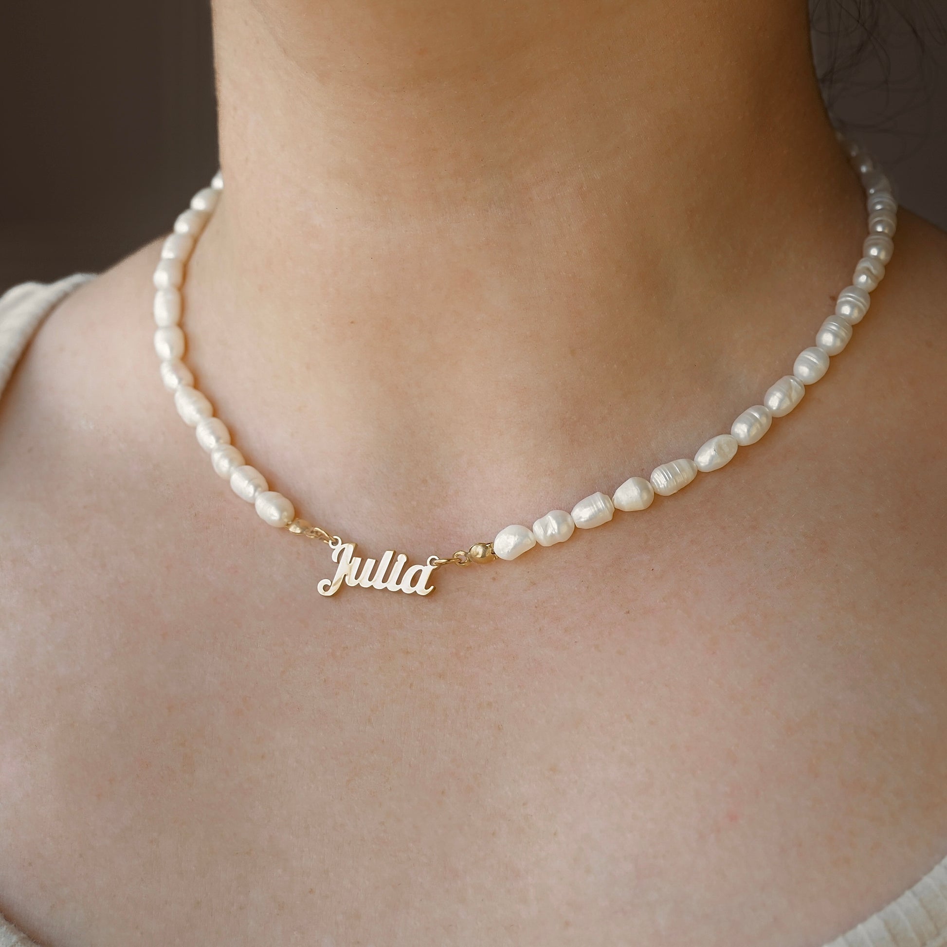 Pearl necklace with a gold name charm on a person's neck