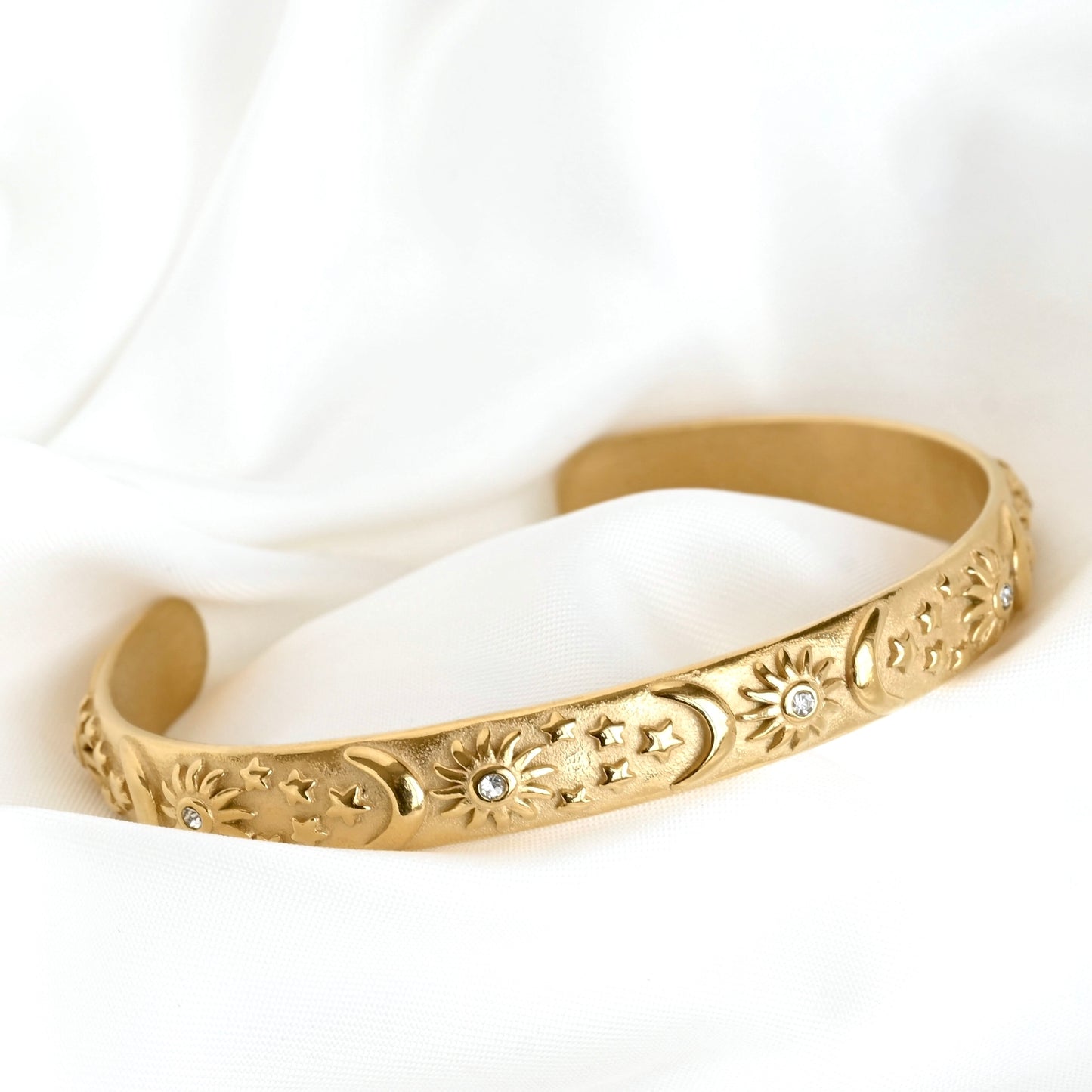 Gold cuff bracelet with sun, moon and star patterns on a white background