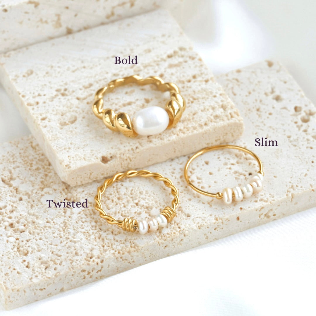 Three gold and pearl rings on a textured stone surface with labels 'Bold', 'Slim', and 'Twisted'.