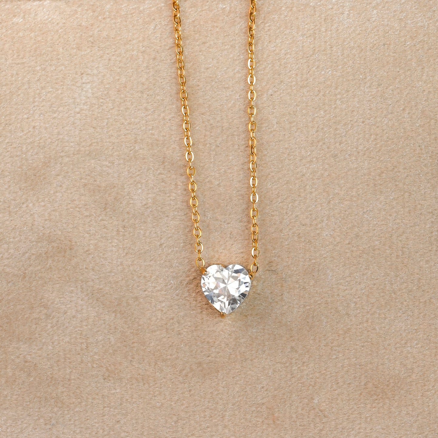 Heart-shaped diamond pendant on a gold chain against a beige background