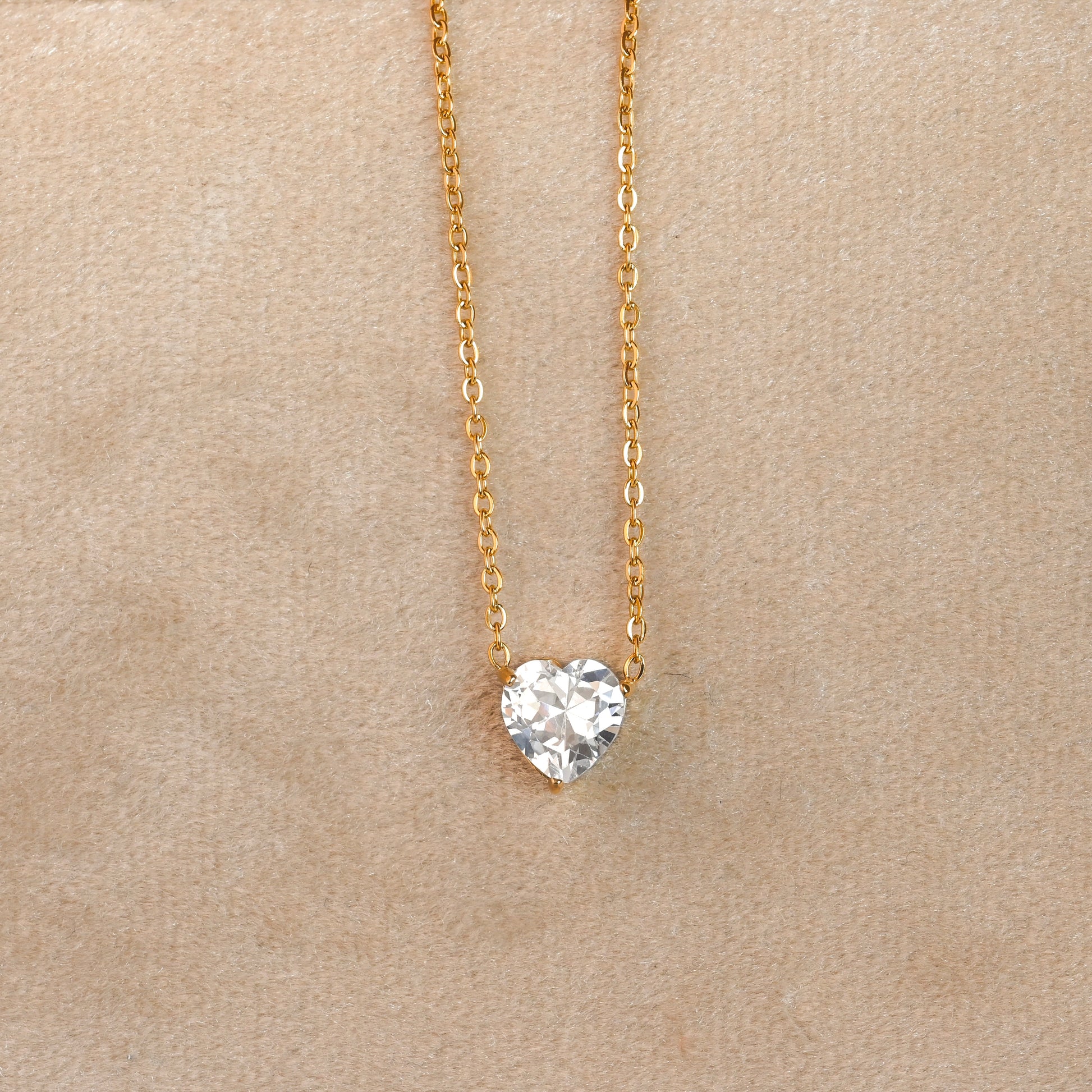 Heart-shaped diamond pendant on a gold chain against a beige background