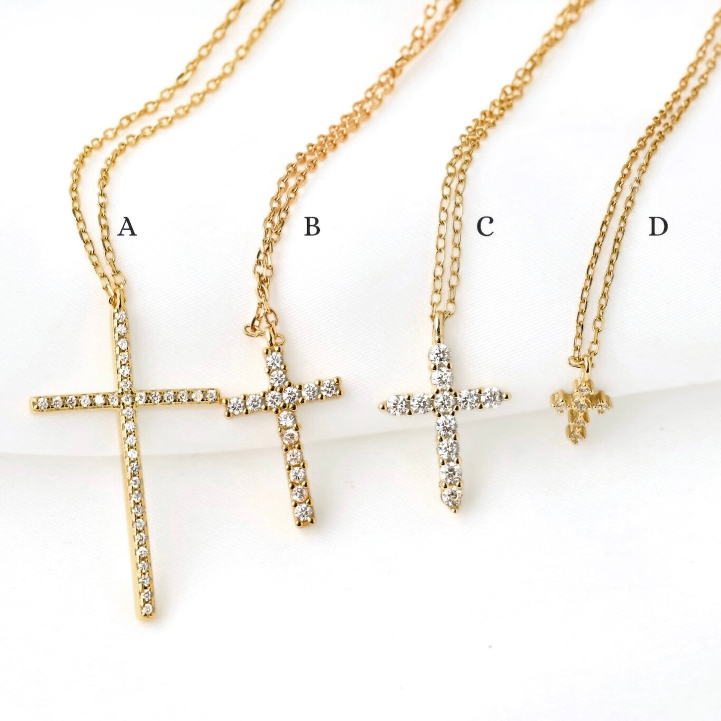 Four gold cross necklaces labeled A, B, C, and D on a white background