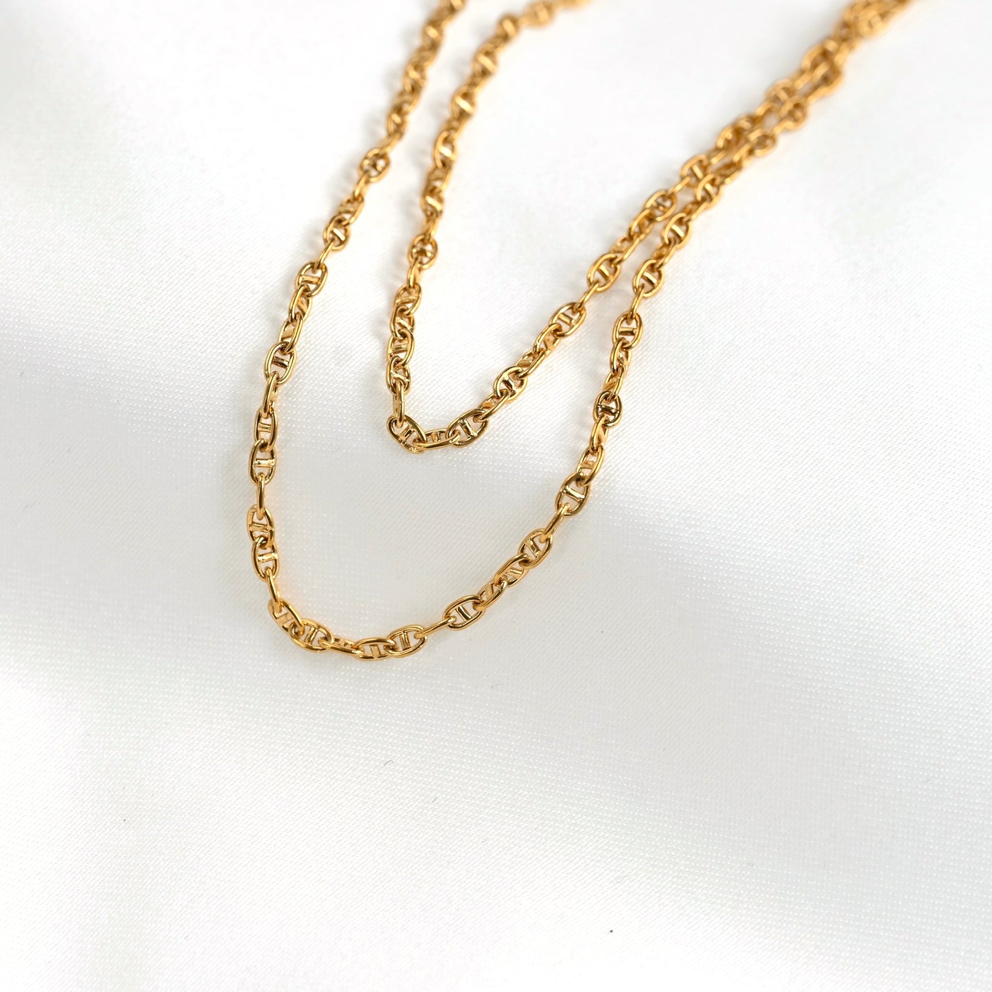 A delicate gold anchor chain draped on a white fabric background.