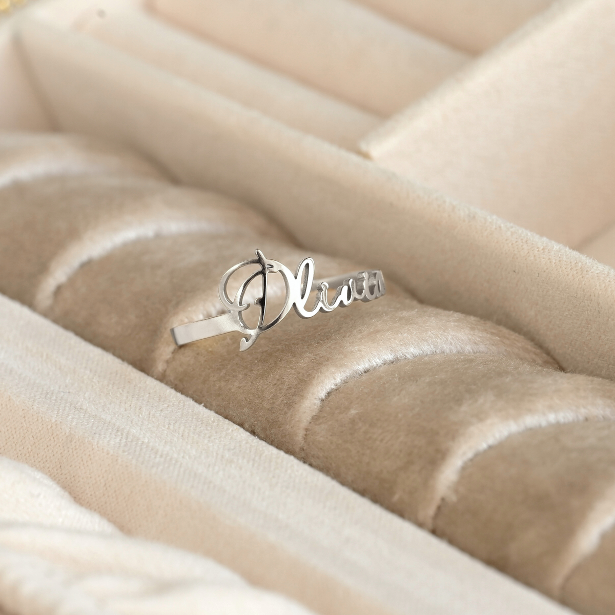 Silver ring with 'Olivia' engraving on a beige quilted surface