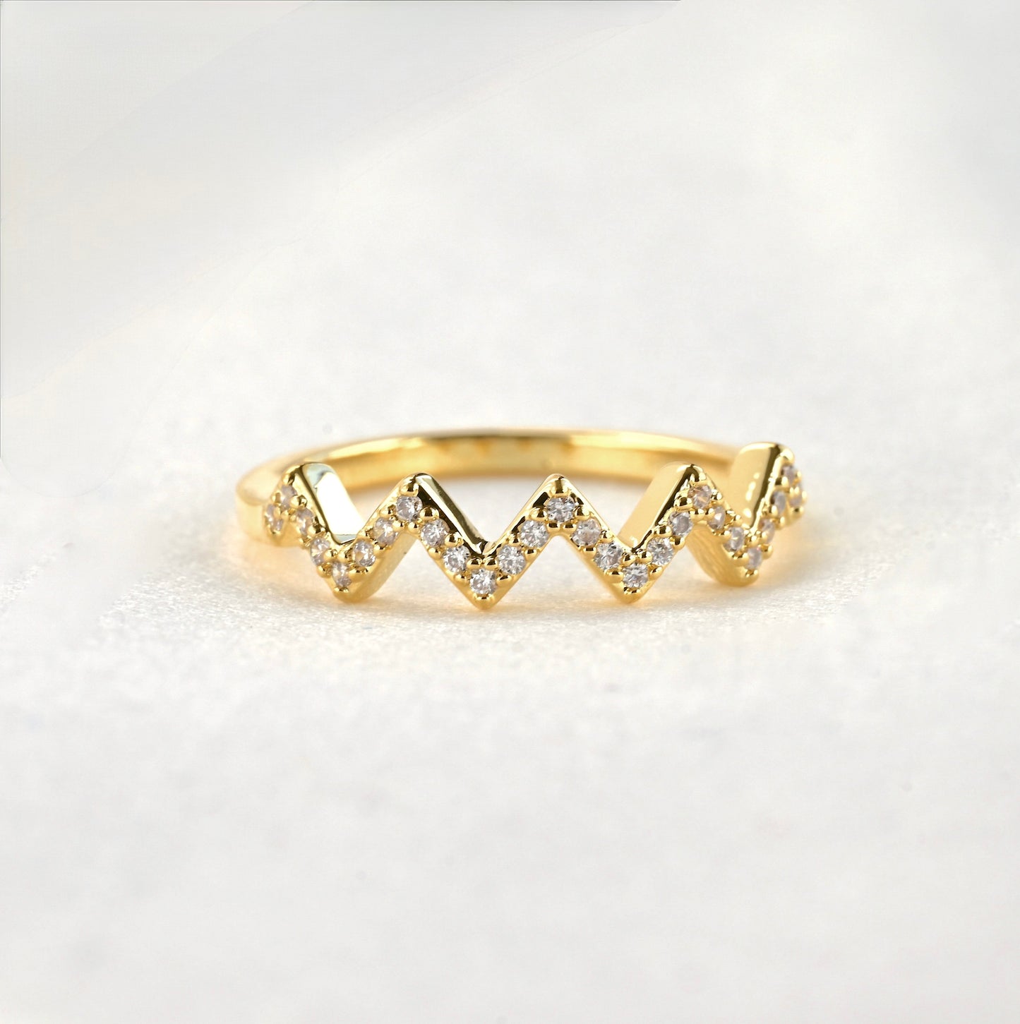 Pave CZ zig zag ring in gold on a white surface.