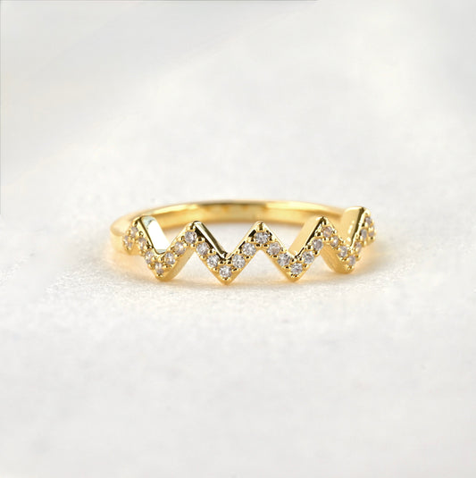 Pave CZ zig zag ring in gold on a white surface.