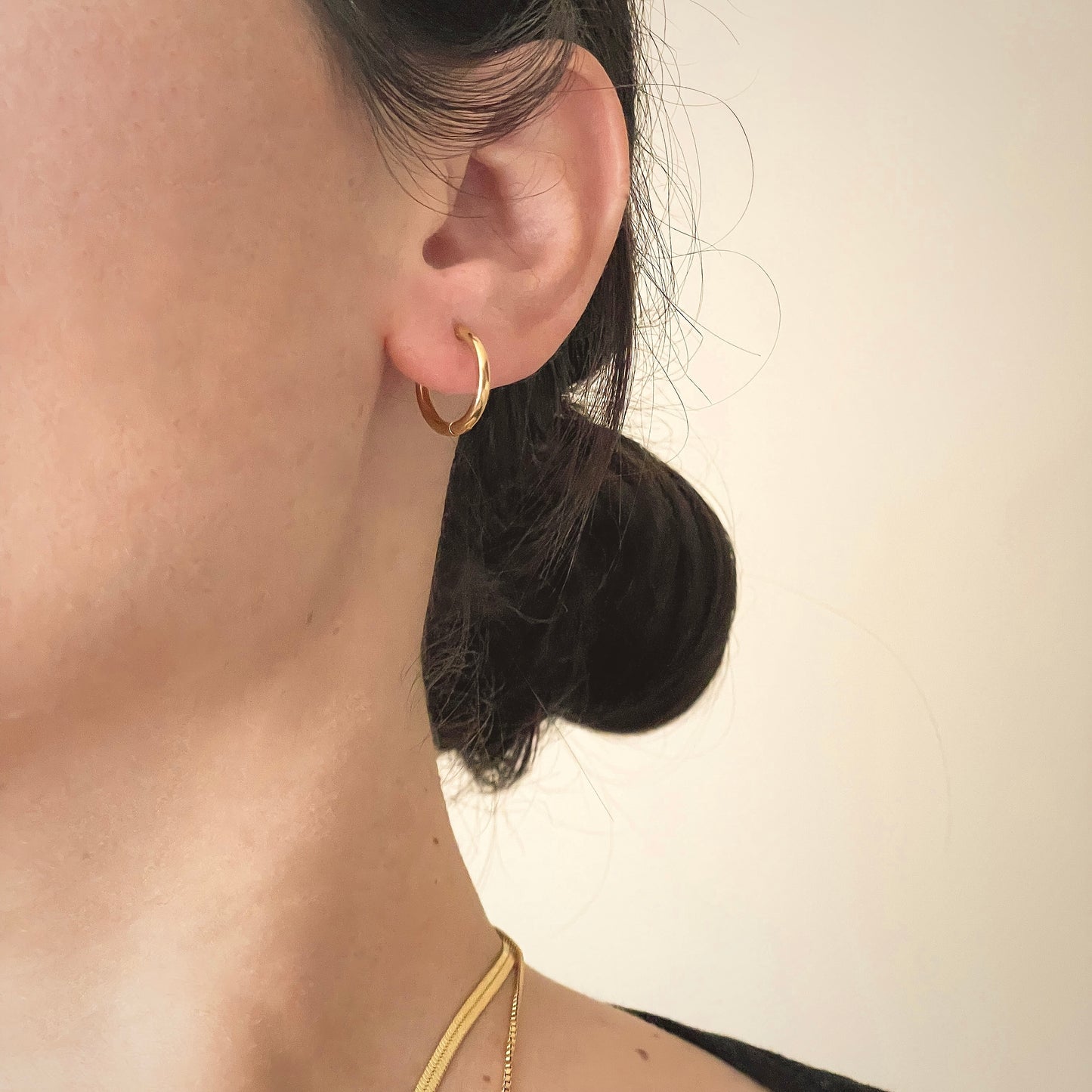 Close-up of a person wearing a gold hoop earring with a neutral background