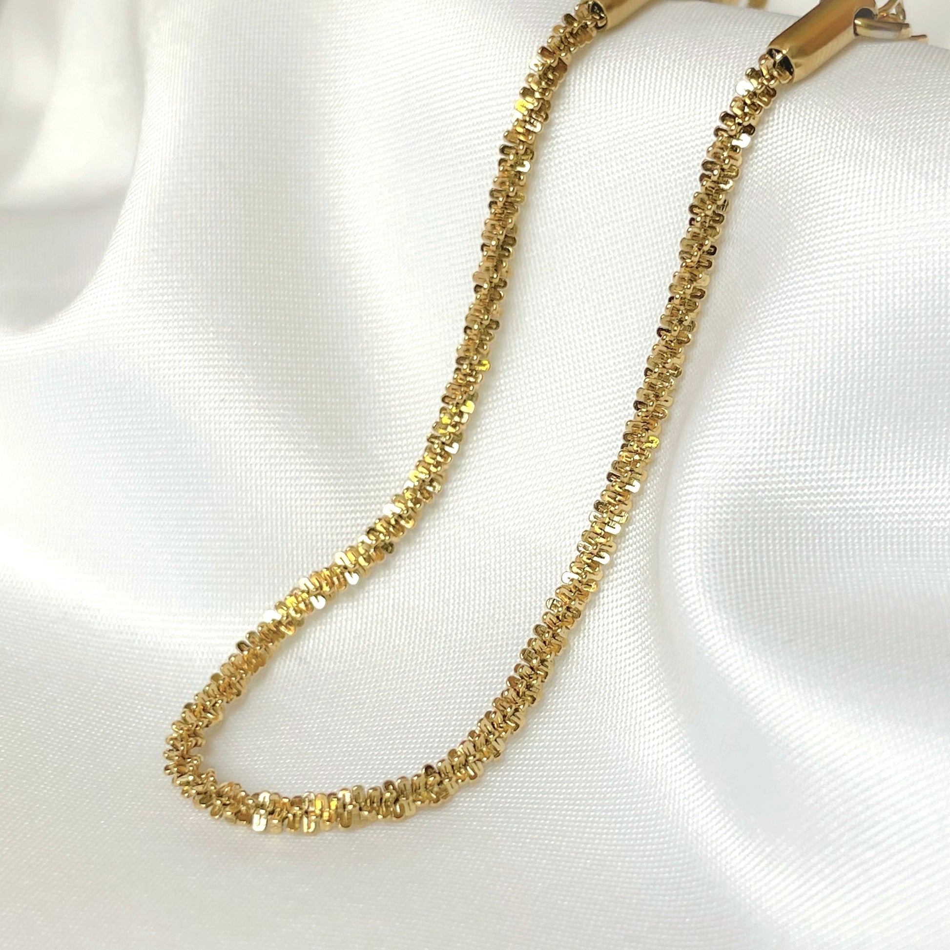 Close up view of gold sparkling rope bracelet  on a white fabric background