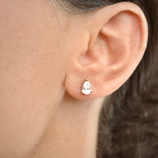 Close-up of an ear wearing a gold teardrop stud earring.