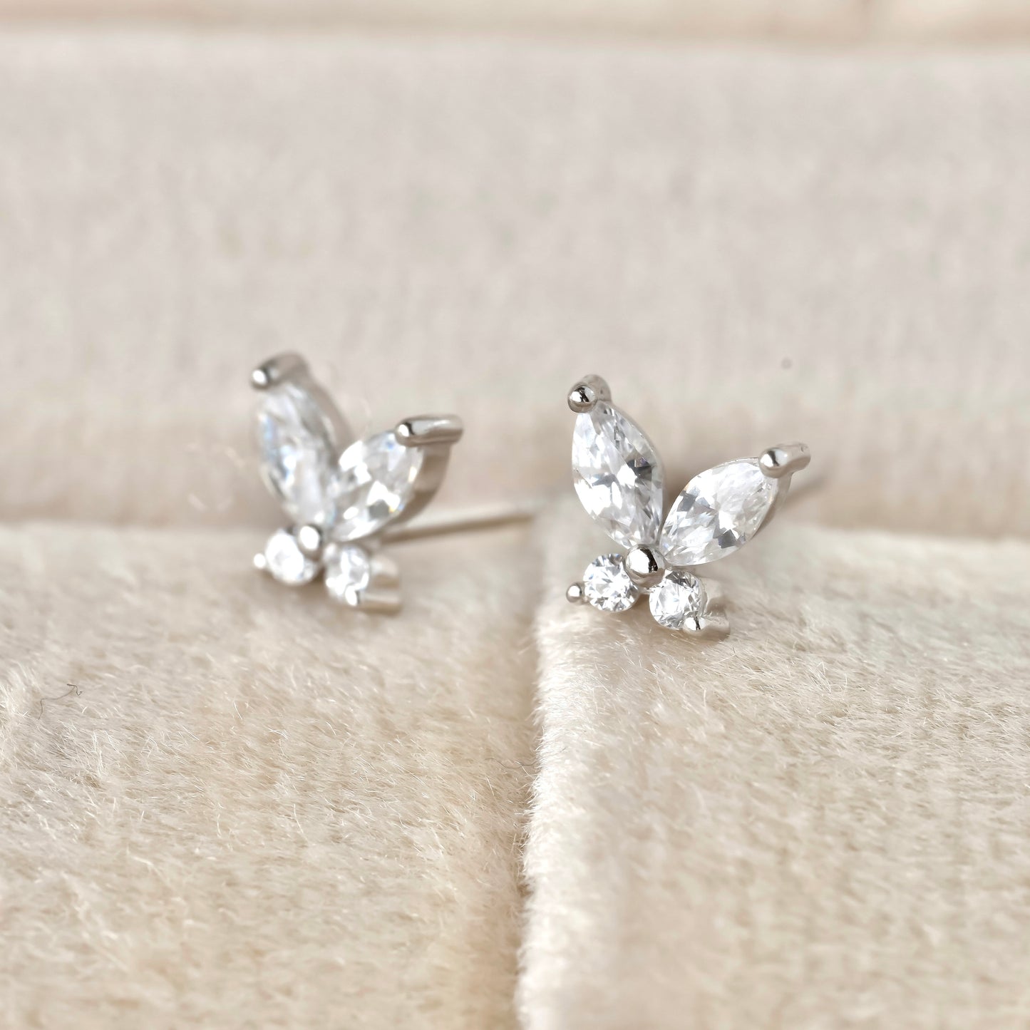 Silver CZ butterfly earrings with clear marquise and round-cut stones on a soft beige fabric background