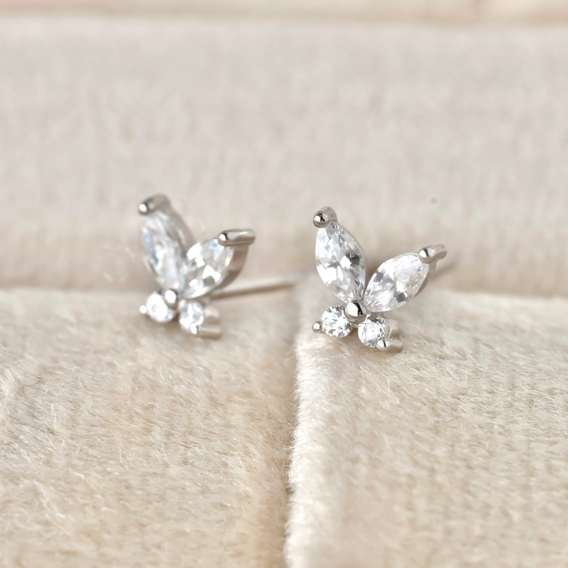 Silver CZ butterfly earrings with clear marquise and round-cut stones on a soft beige fabric background