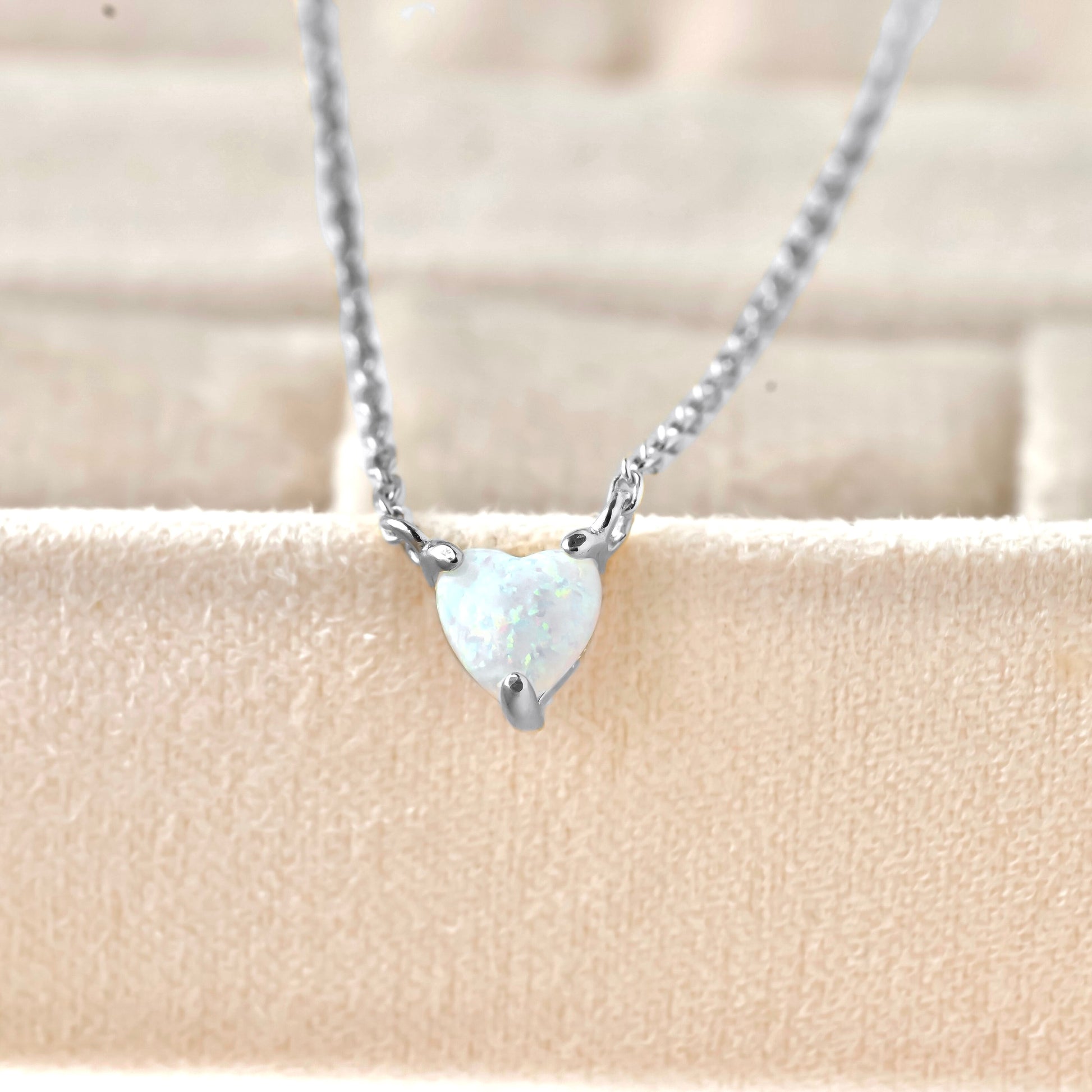 Silver necklace with a heart-shaped opal pendant on a beige background