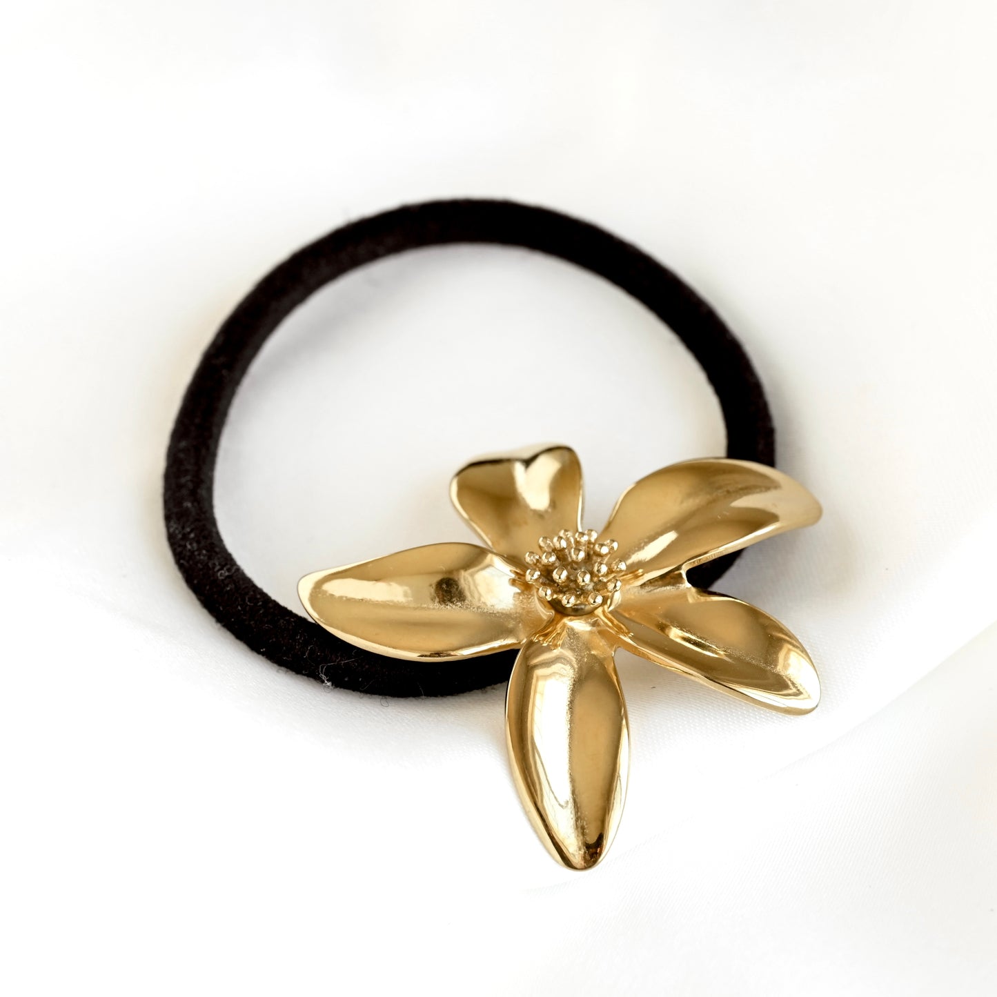 A black elastic hair tie with a shiny gold flower-shaped charm, photographed on a clean white background.