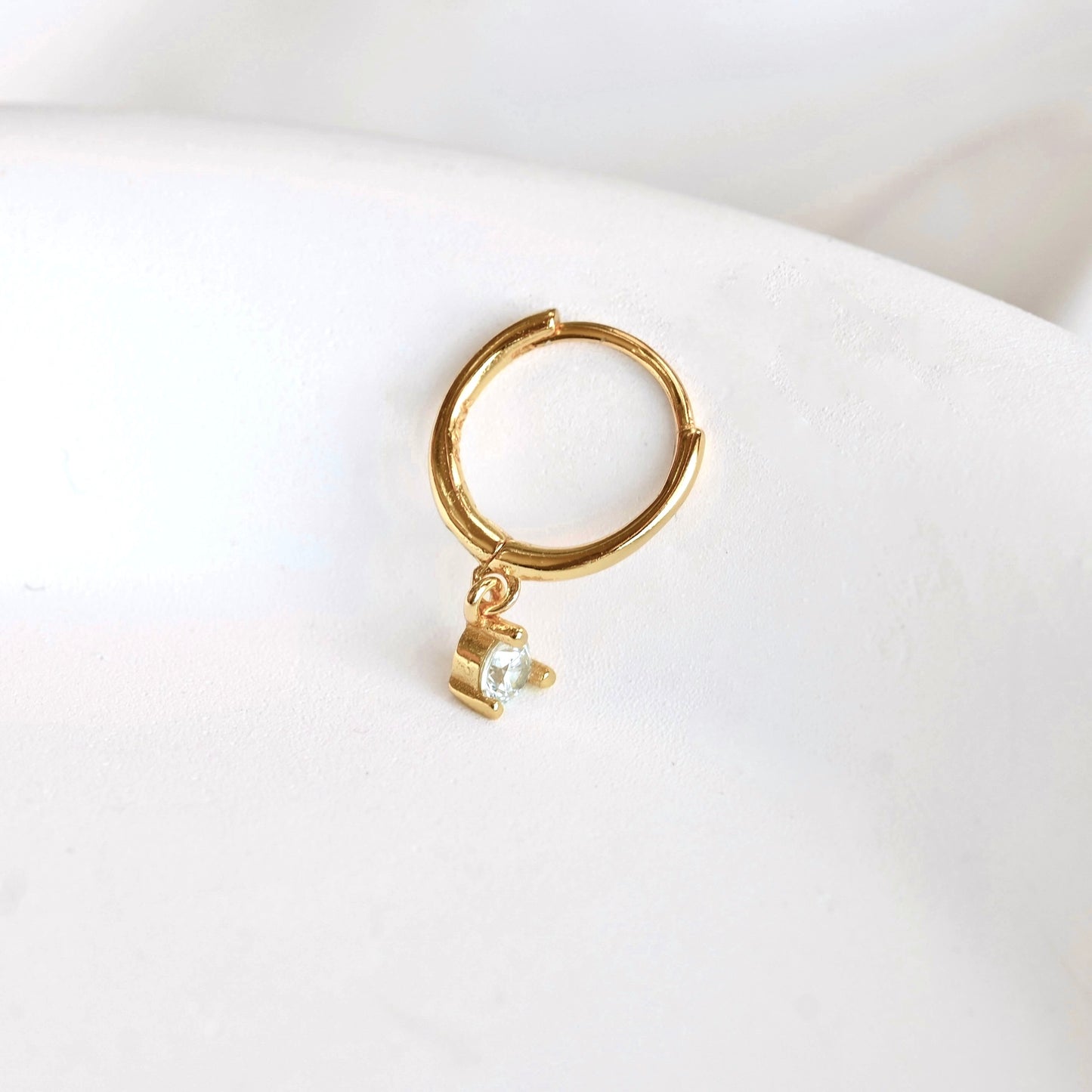 Tiny gold hoop earring with a small charm on a white trinket dish.