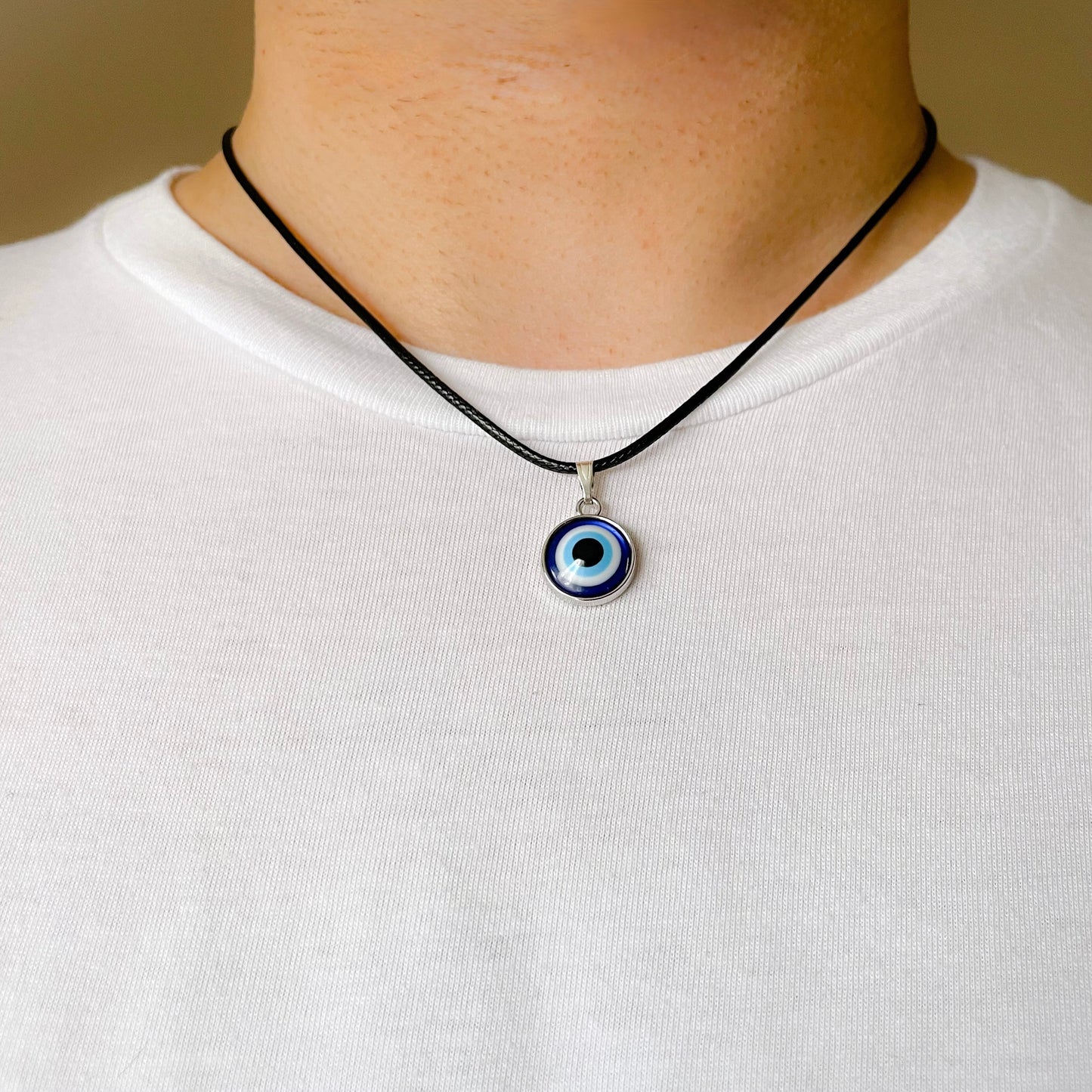 Black cord necklace with an evil eye pendant worn by a man on a white shirt