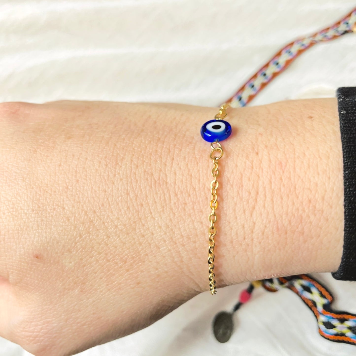 Side view of gold chain bracelet with a blue evil eye charm on a wrist.
