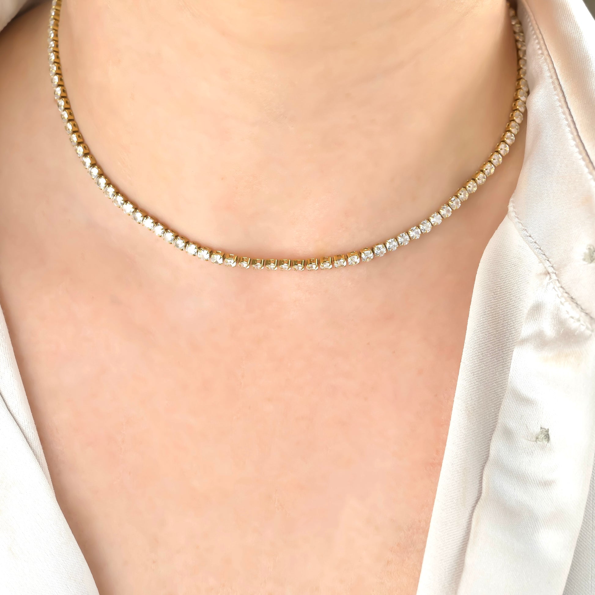 Close-up of a diamond necklace on a person wearing a white satin shirt.