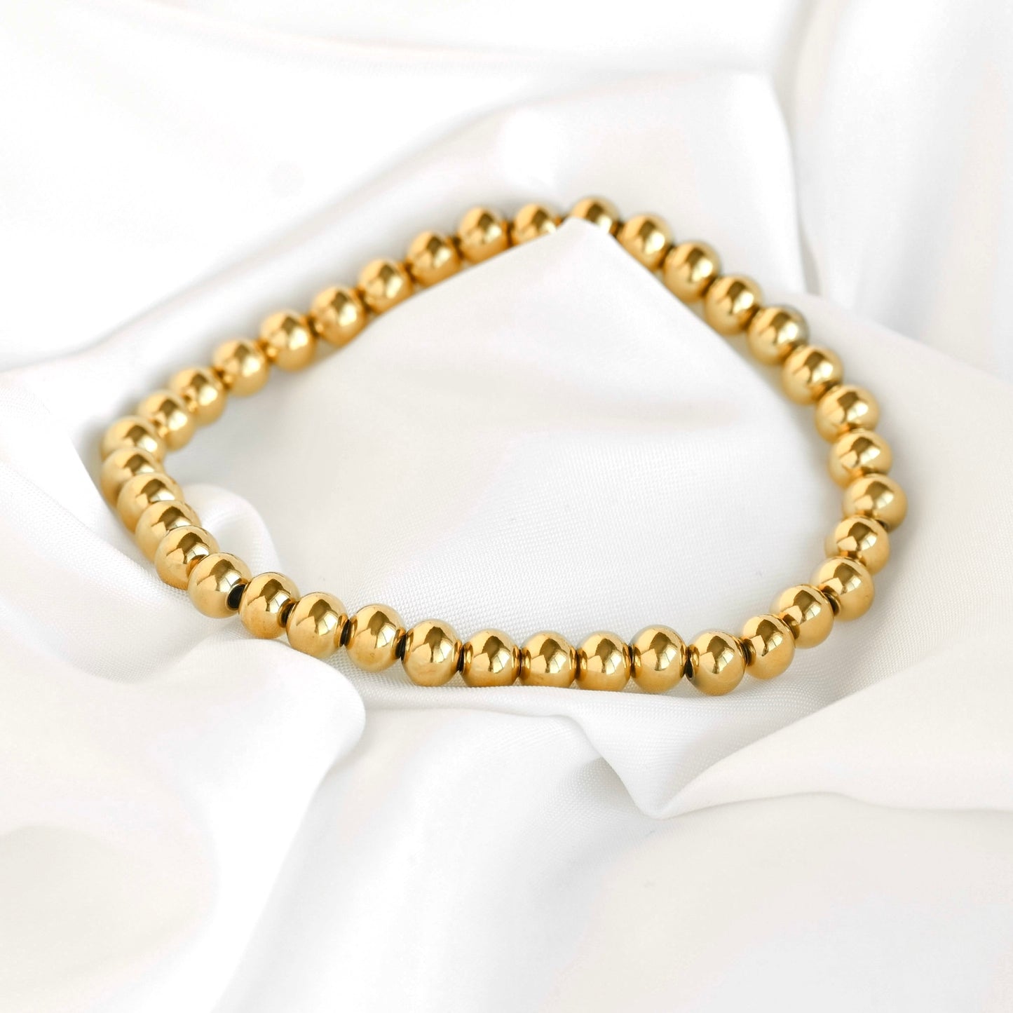 Gold ball bead bracelet on a white fabric background