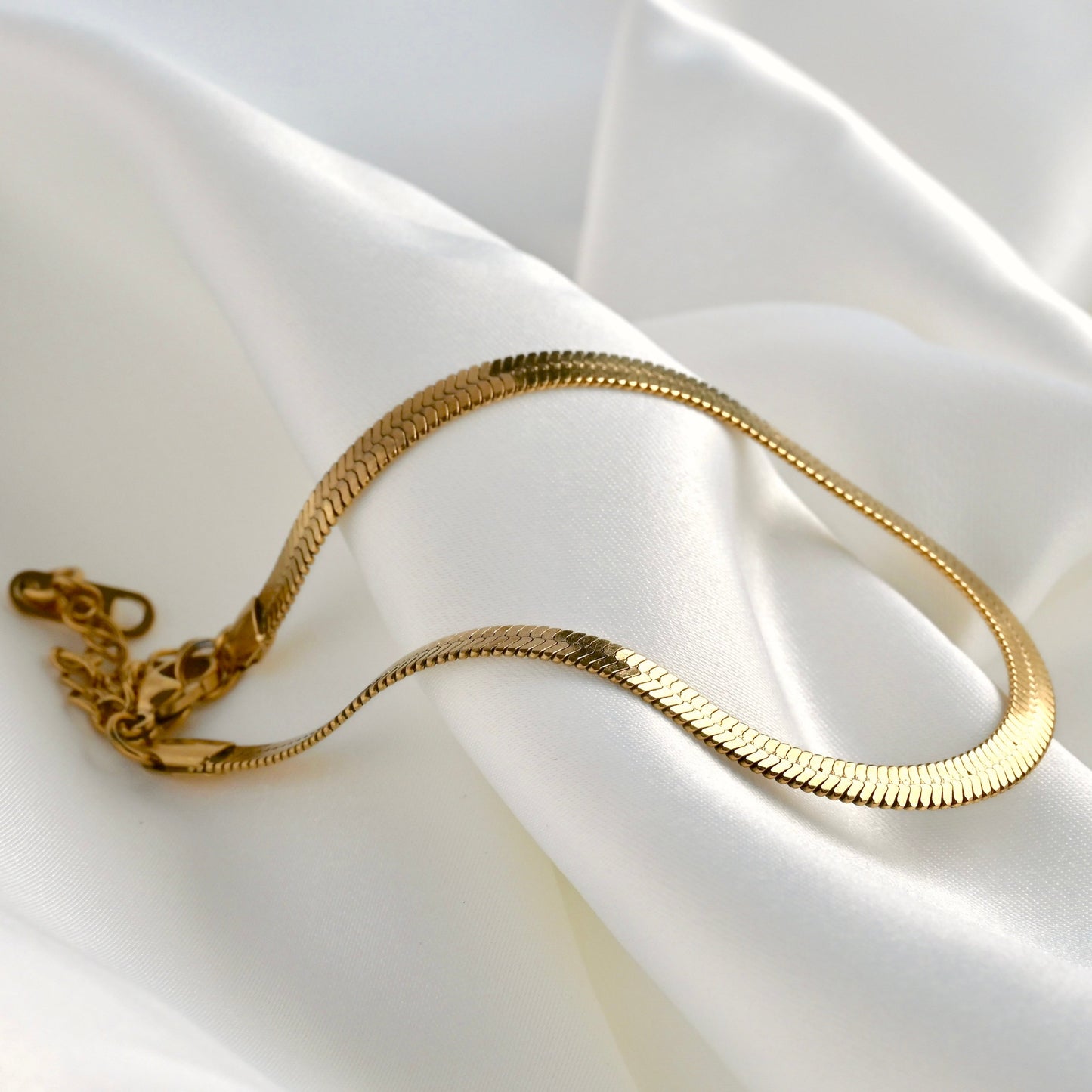 Gold herringbone chain anklet on a white fabric background
