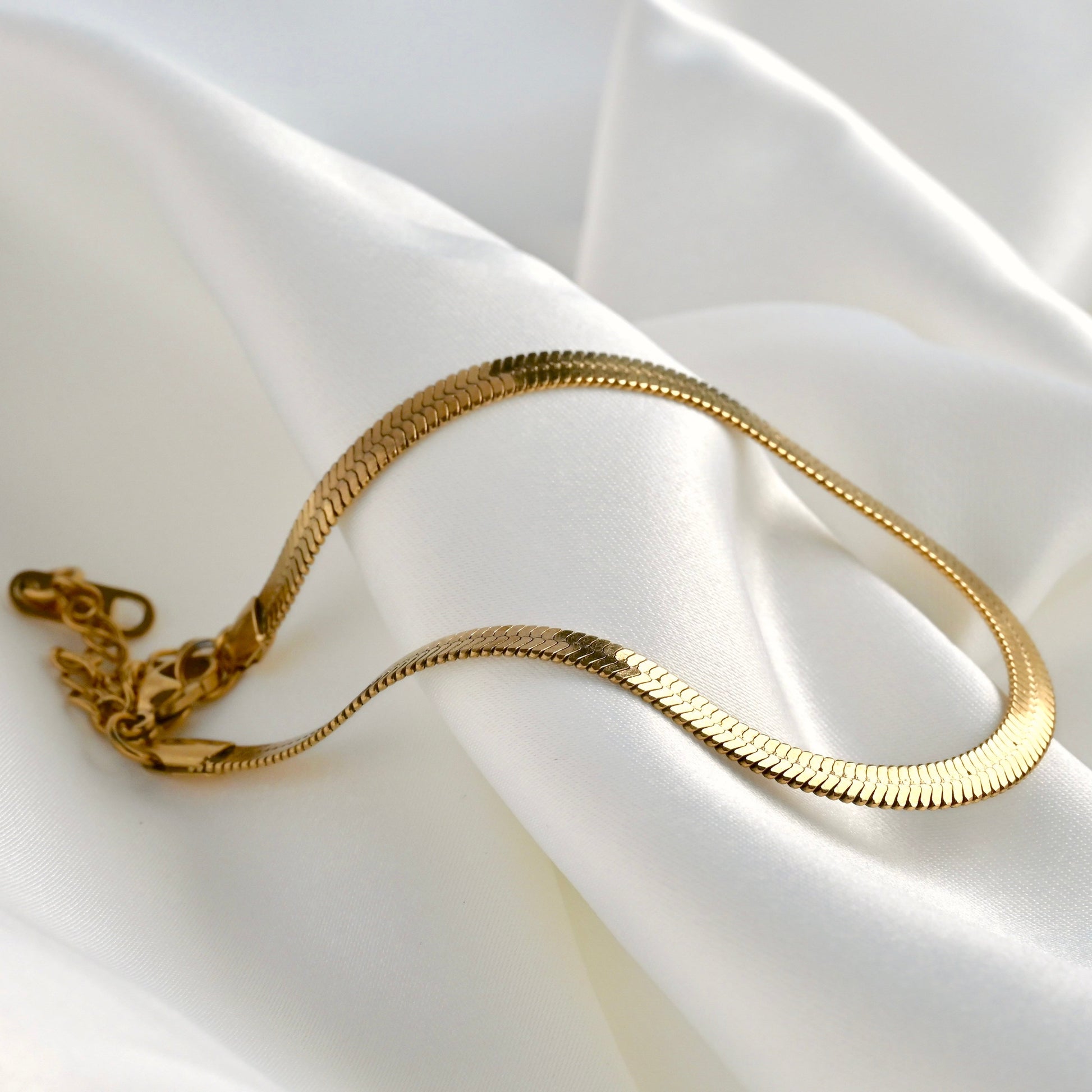Gold herringbone chain anklet on a white fabric background