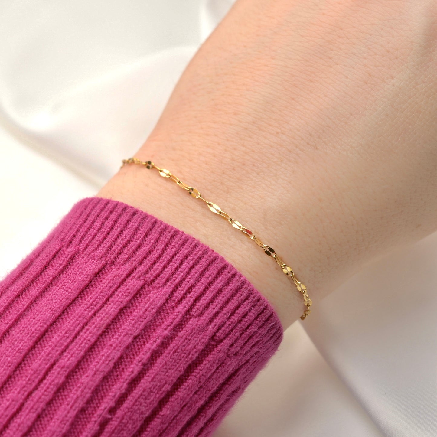 Gold bracelet on a wrist with a pink sleeve against a white background