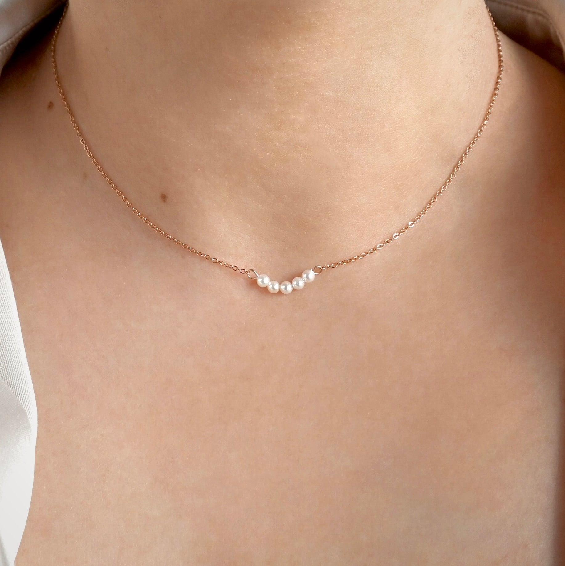 Front view of pearl necklace with a dainty rose gold cable chain on a person's neck with a neutral background
