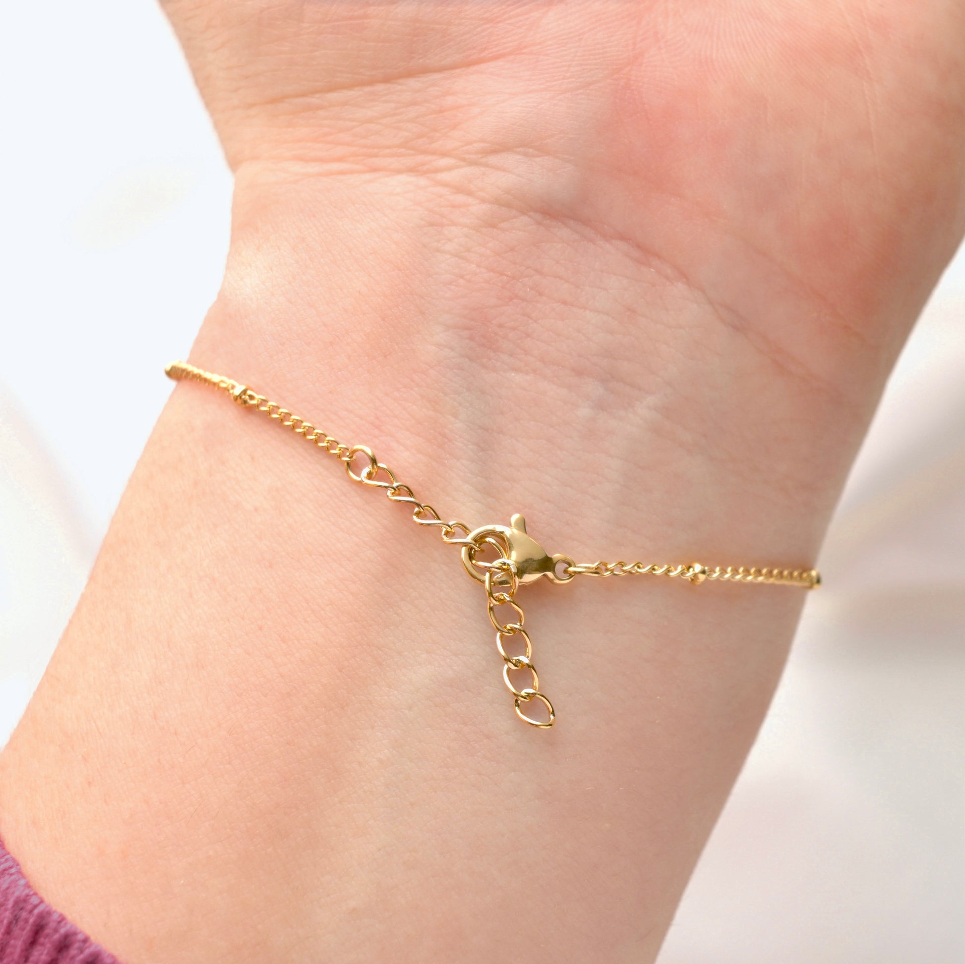 Gold satellite bracelet on a person's wrist with a blurred background