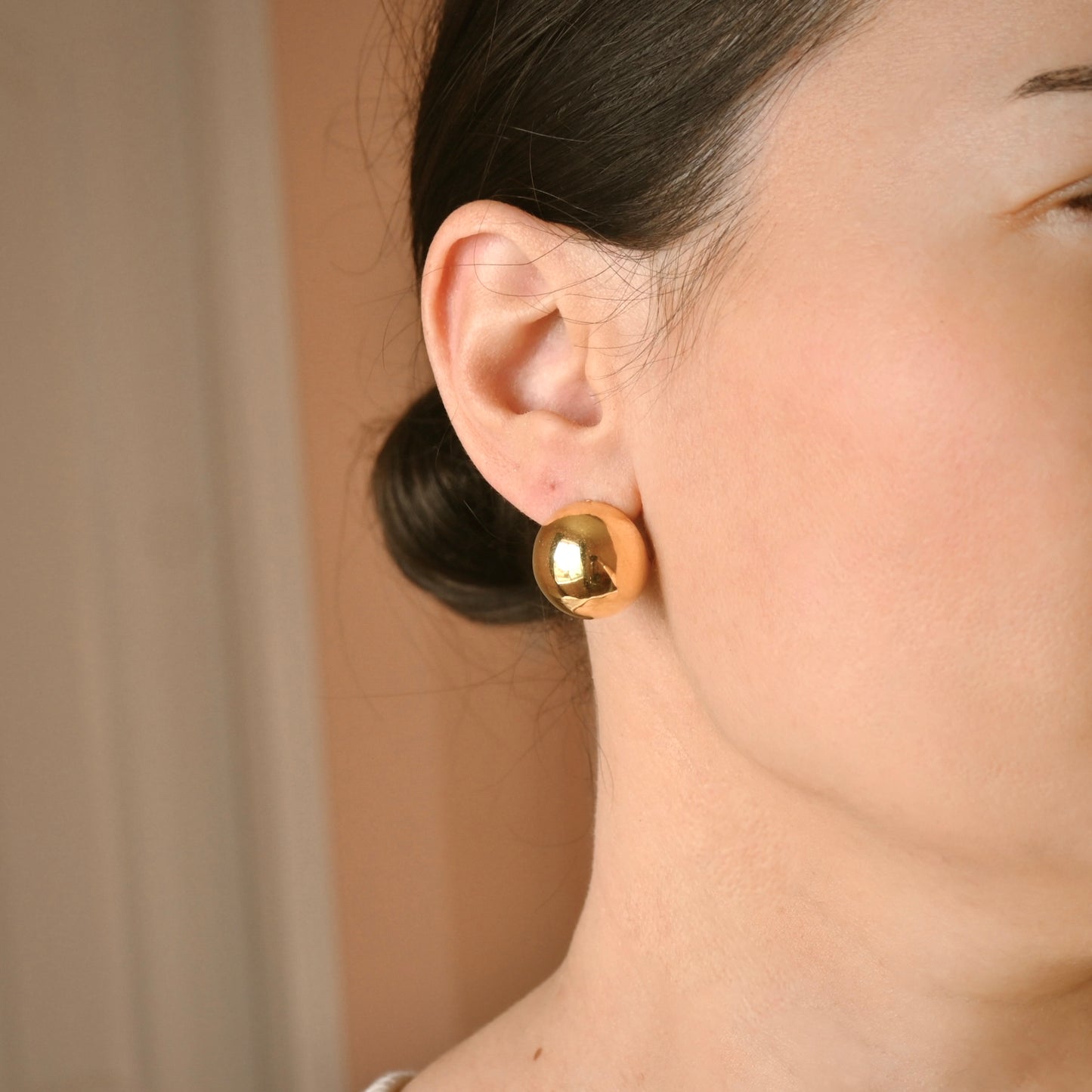 A close-up side profile of a woman wearing a single polished gold spherical stud earring.