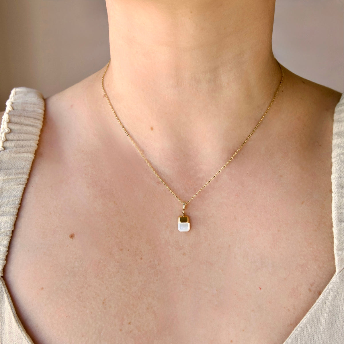 A delicate gold pearl necklace with a small white rectangular pendant featuring a gold accent, shown worn on a model's neck.