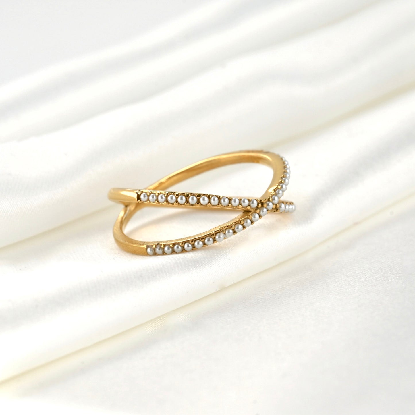 Angled view of half eternity criss cross gold ring with tiny simulated pearls on a white satin background