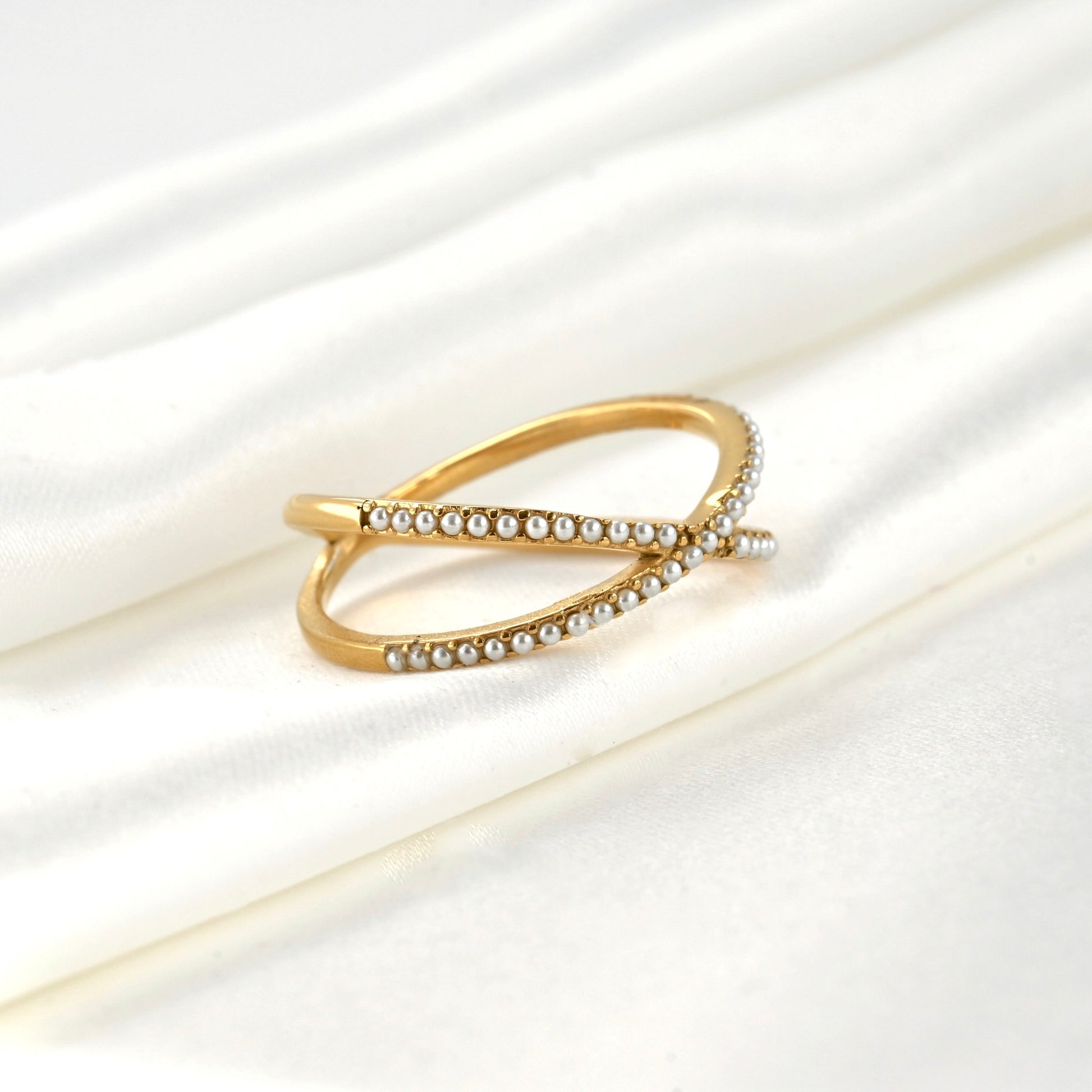 Angled view of half eternity criss cross gold ring with tiny simulated pearls on a white satin background