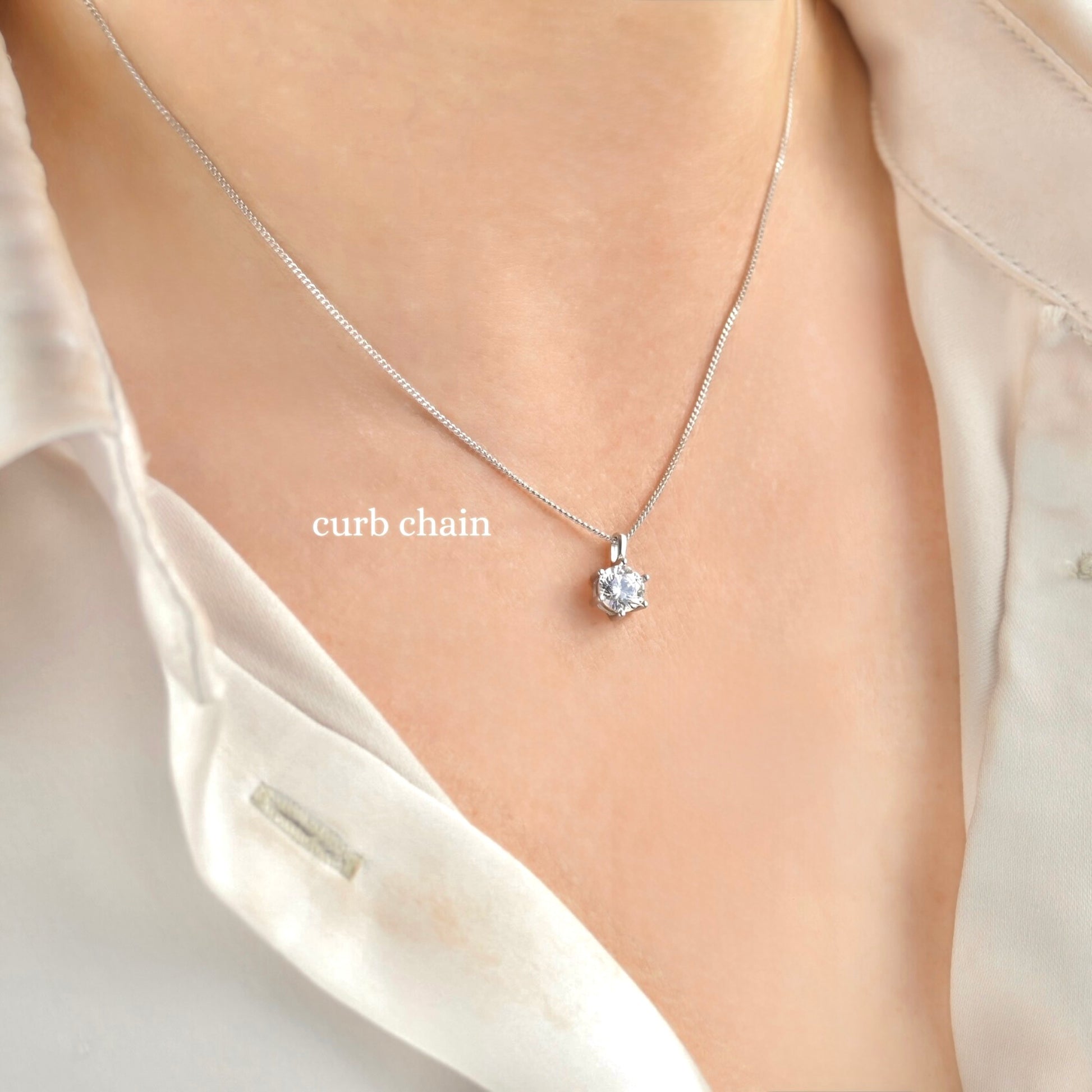 Silver fine curb necklace with a pendant on a person wearing a light-colored shirt.