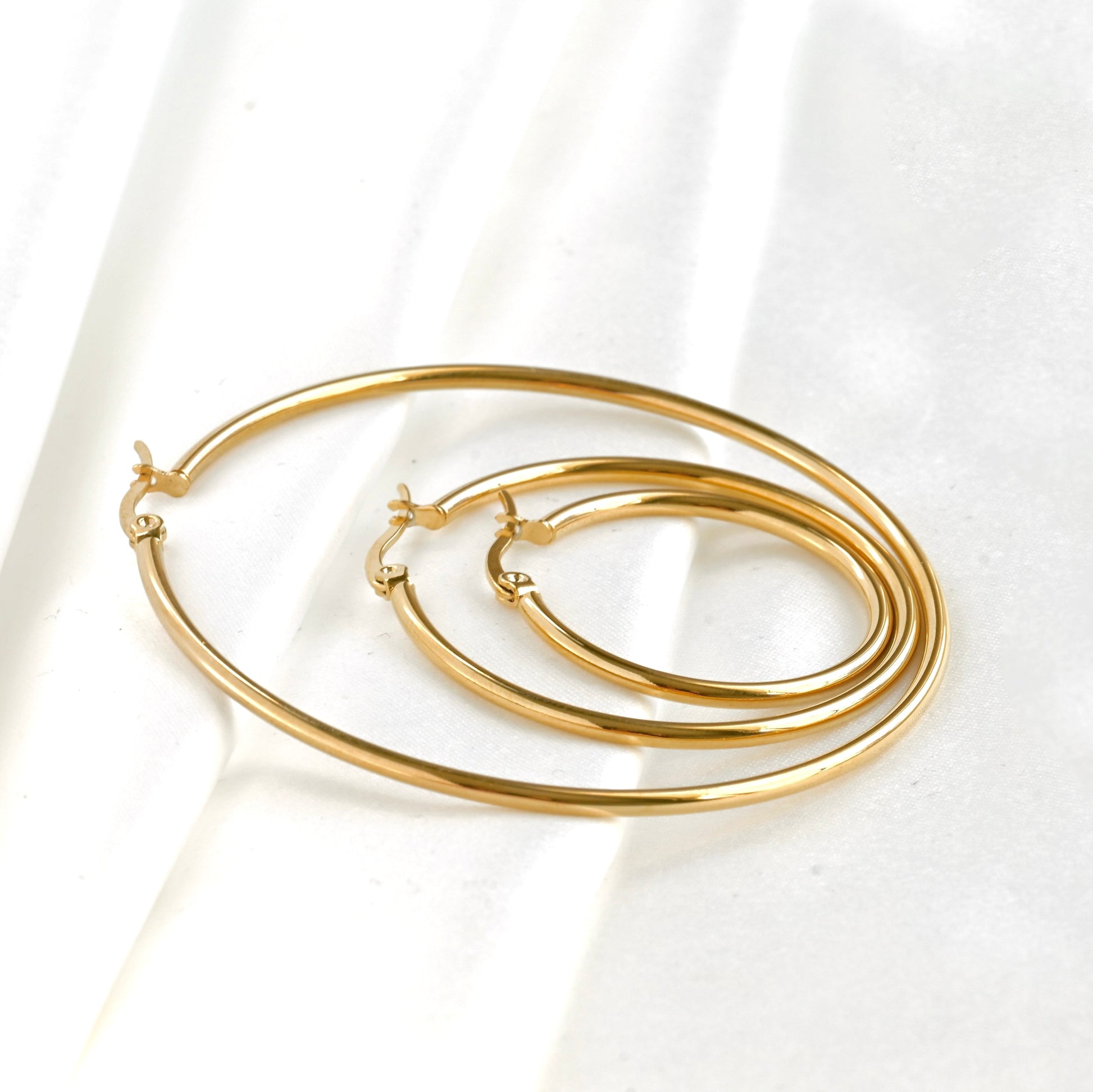 Set of gold hoop earrings in graduated sizes on a white fabric background