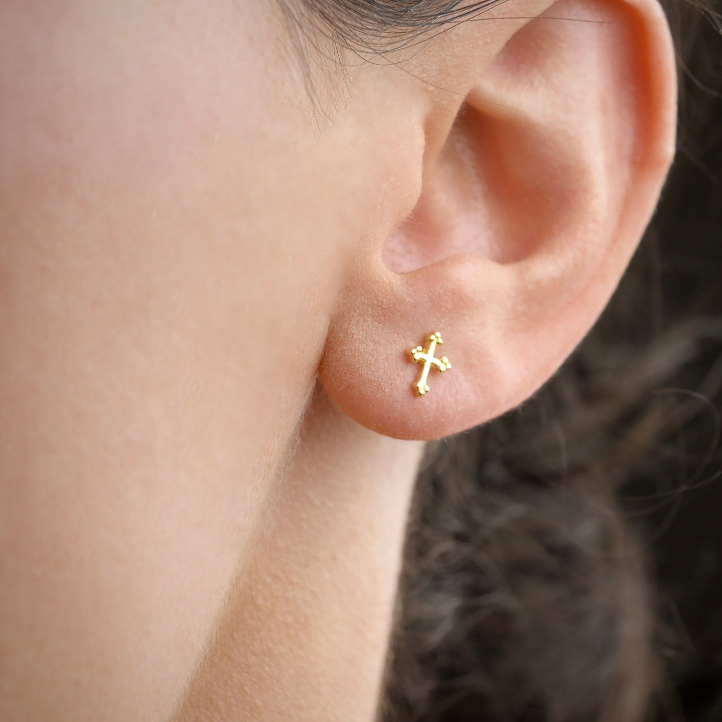 Gold cross earring on a person's ear with a blurred background