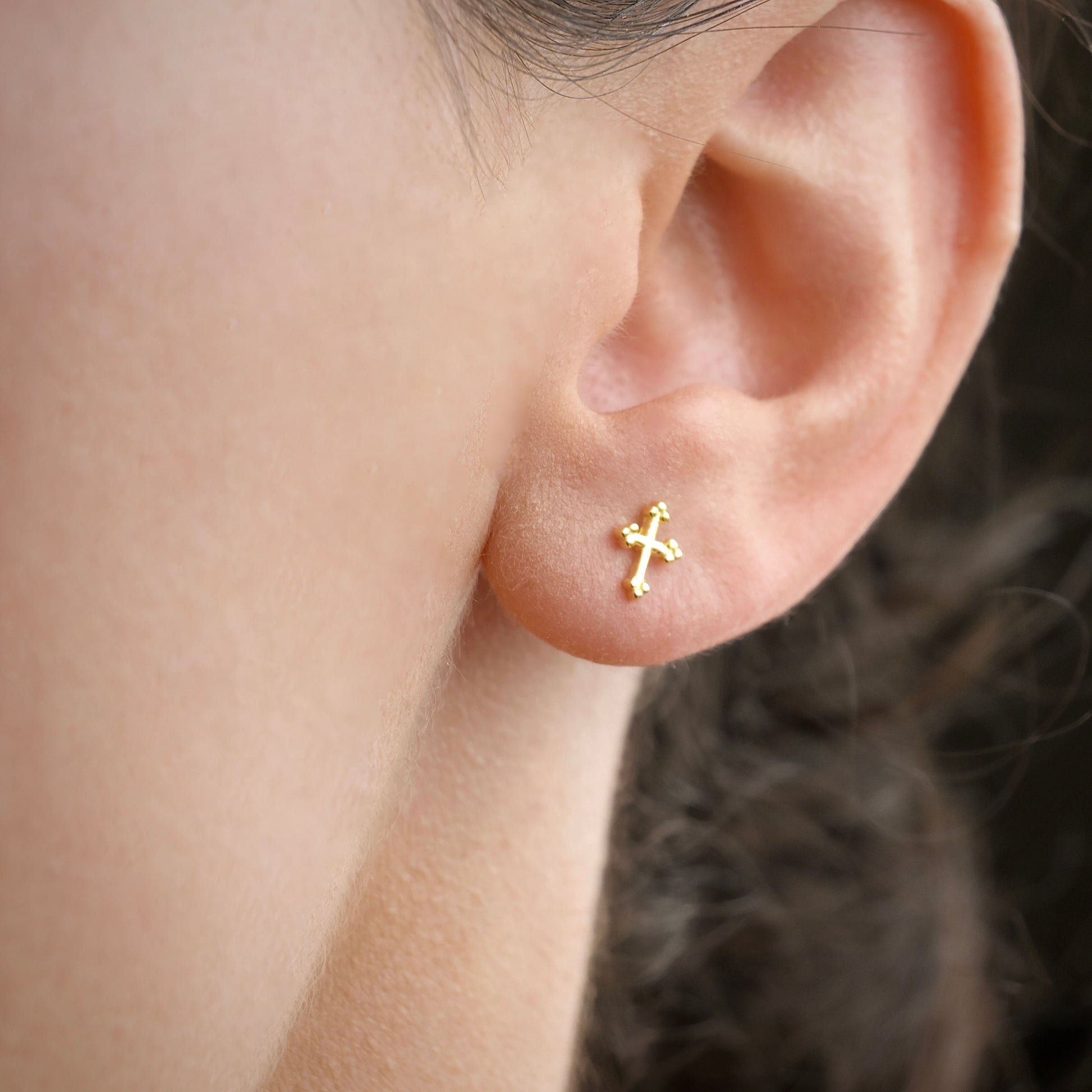 Gold cross earring on a person's ear with a blurred background
