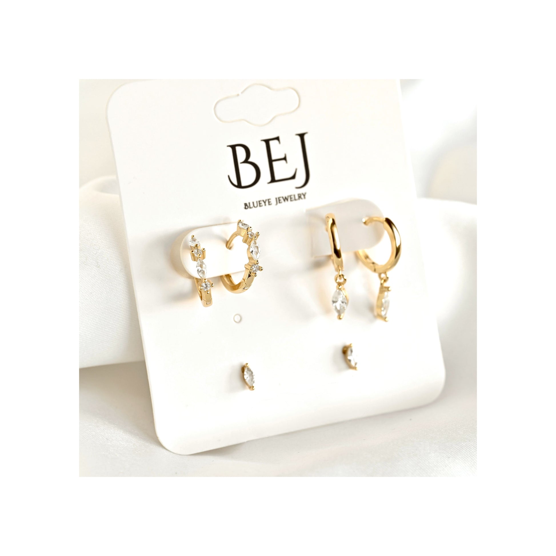 A pair of gold huggie hoop earrings with clear crystal accents and matching small stud earrings, displayed on a white card labeled BEJ Marine Jewelry.